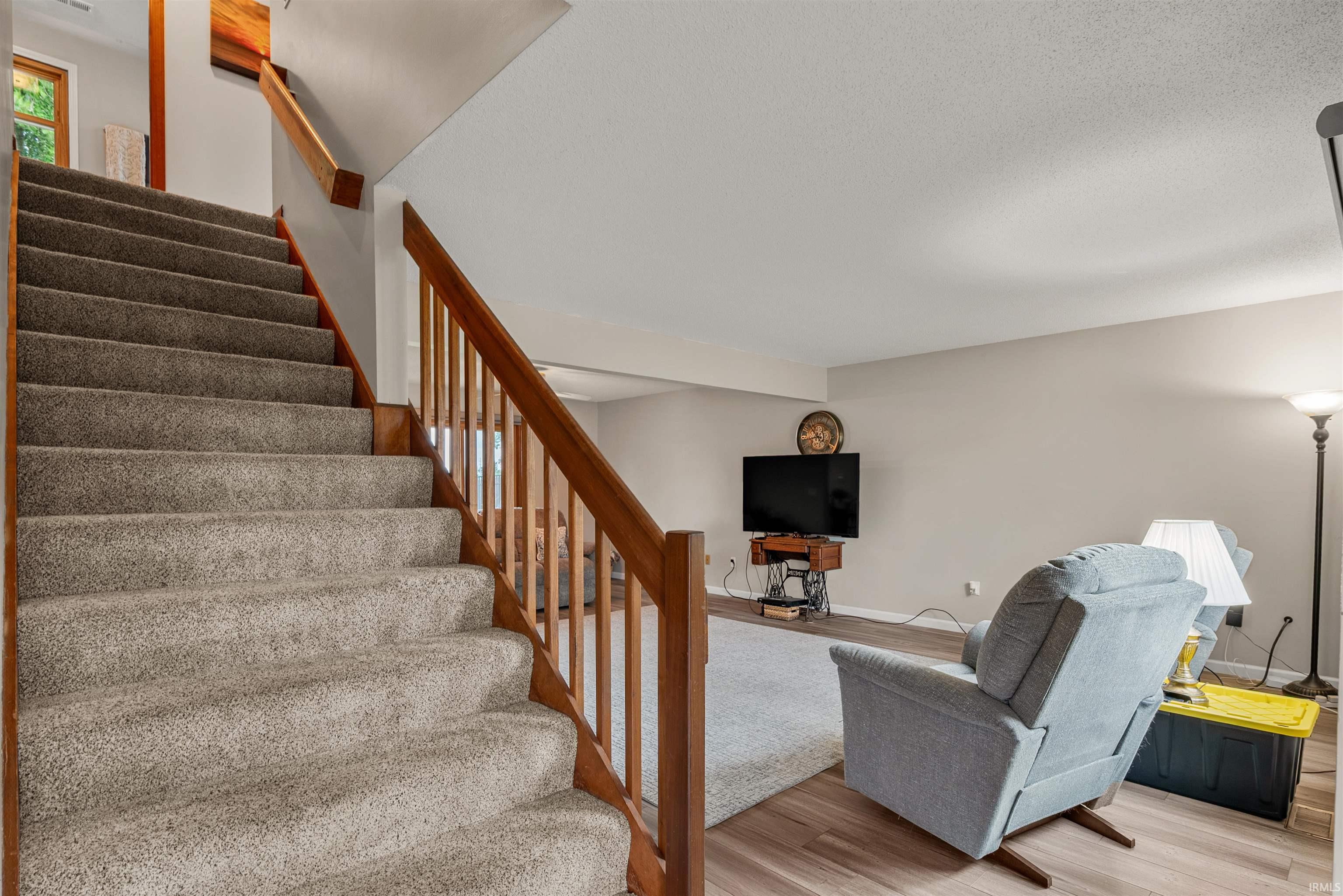 Carpeted staircase with wood-finish handrails and balusters, opening to a living area with wood-finish flooring