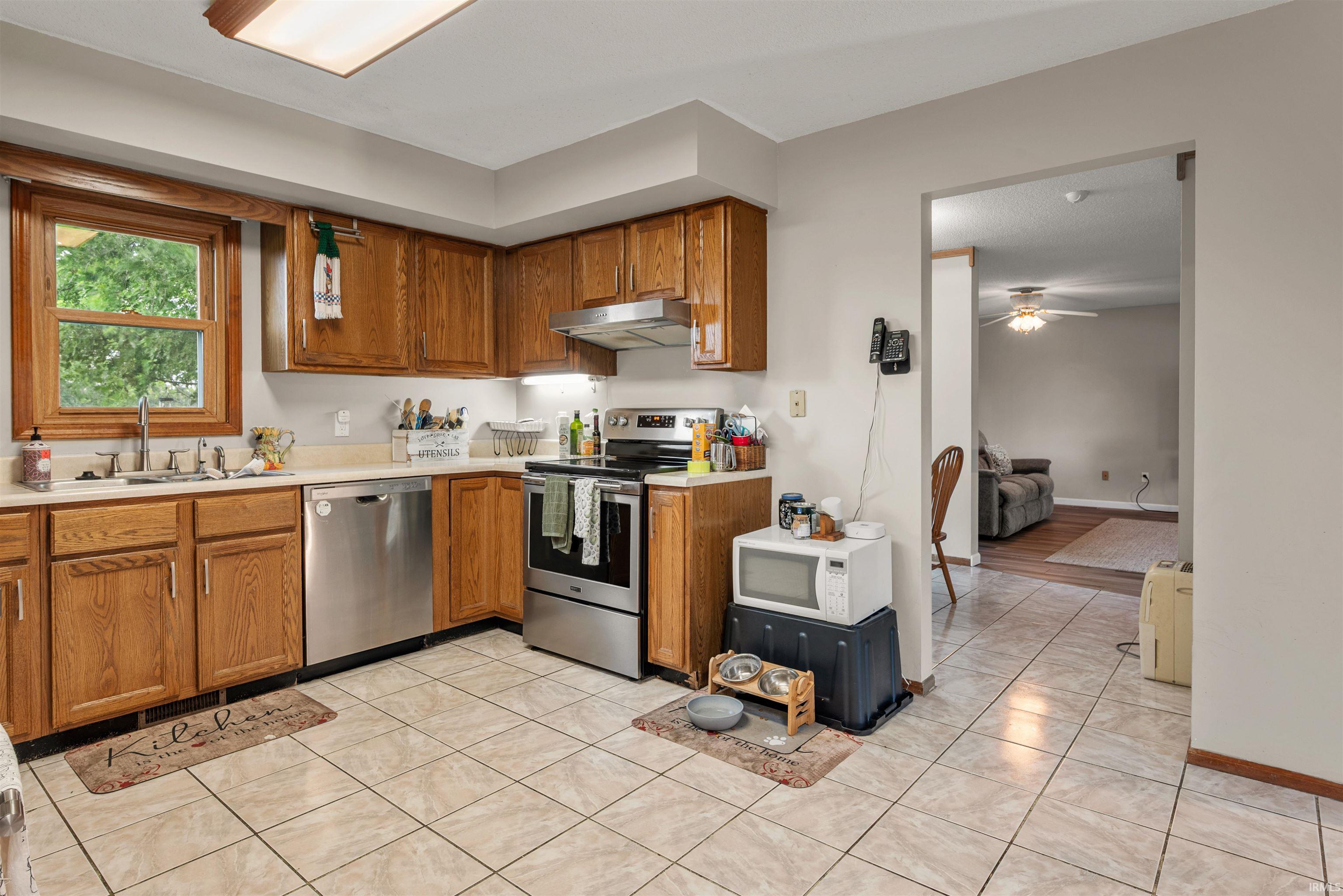 Kitchen featuring wood cabinetry, stainless steel appliances, a stainless steel sink, tile flooring, and a window above the sink