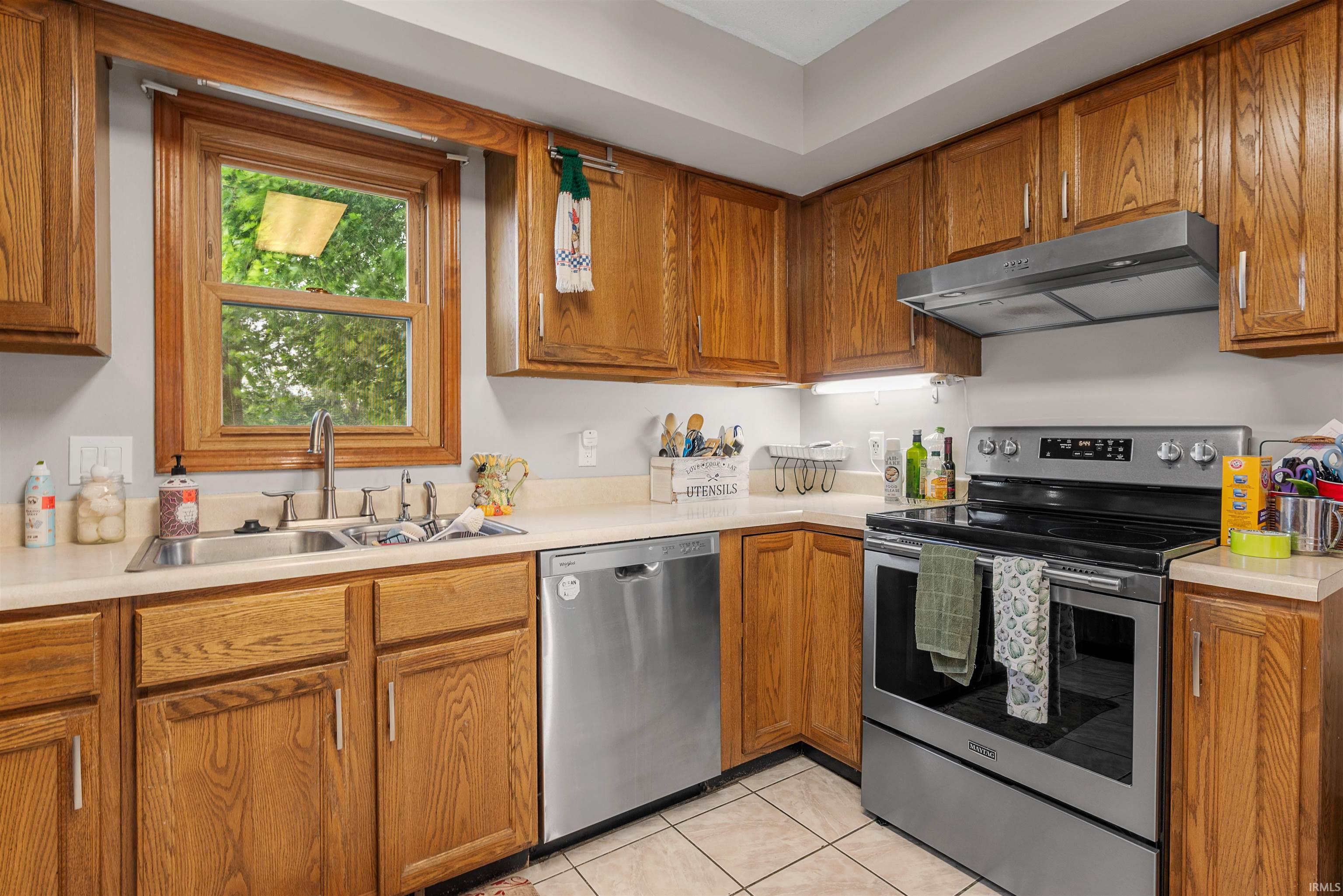 Kitchen featuring wood cabinetry, light-toned countertops, a stainless steel sink with a goose-neck faucet, and stainless steel appliances including a range and dishwasher
