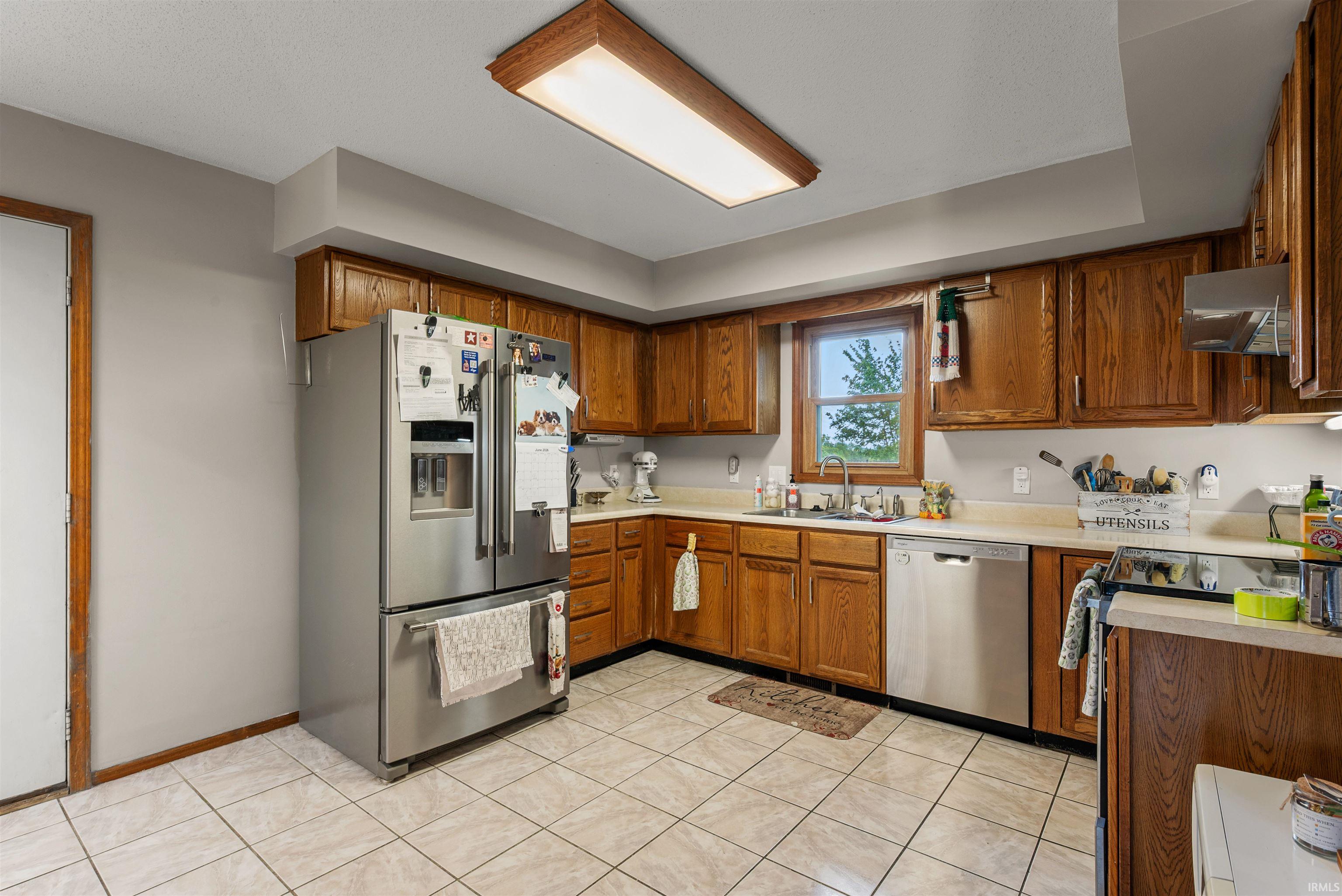 Kitchen featuring tile flooring, wood-finish cabinetry, stainless steel appliances, and a window above the sink