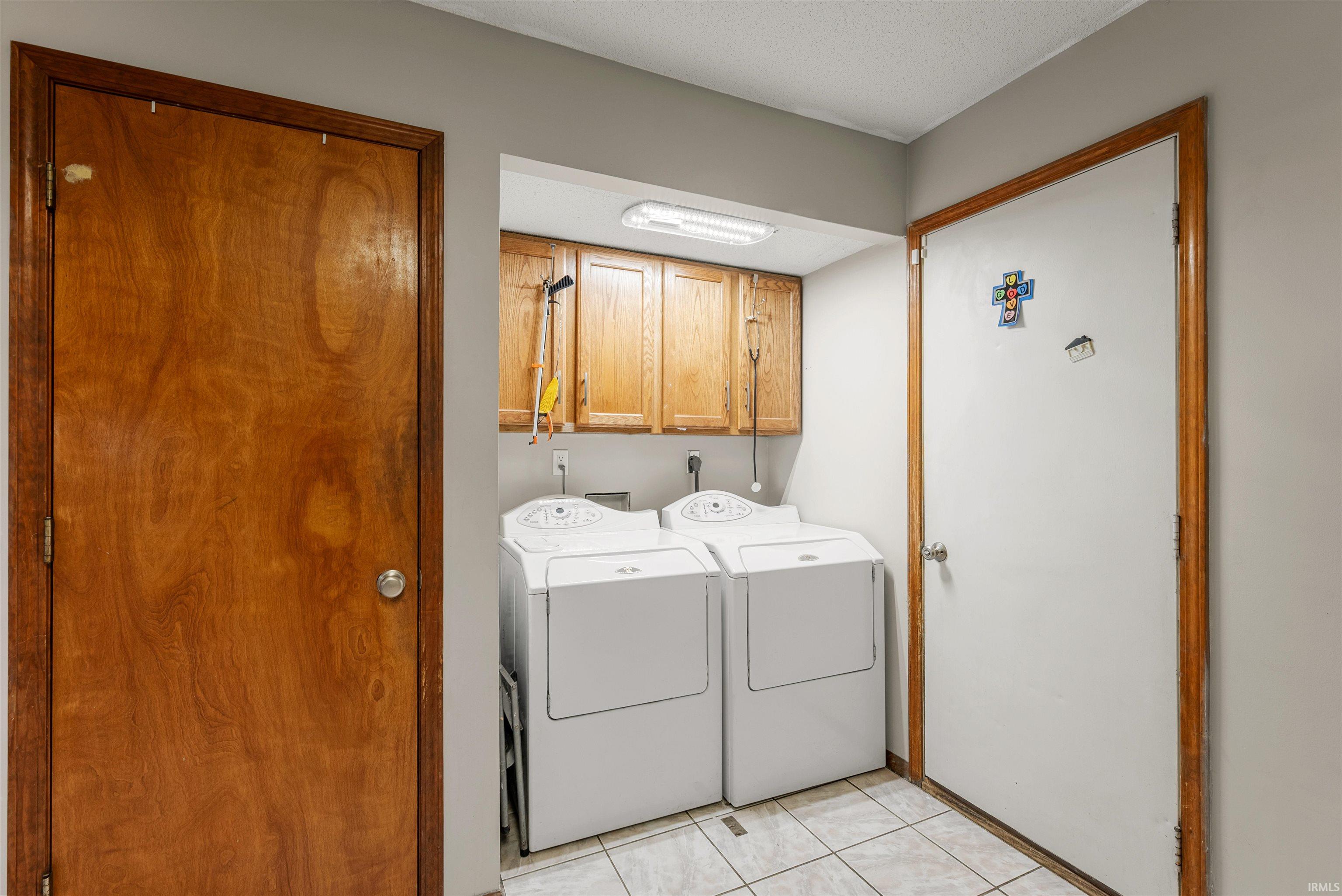 Dedicated laundry area featuring tile flooring, wood cabinetry, and a fluorescent ceiling light fixture