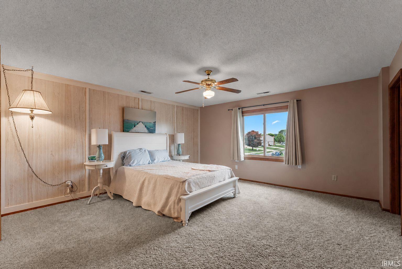 Spacious room featuring neutral carpeting, a ceiling fan with integrated lighting, and a large window offering natural light