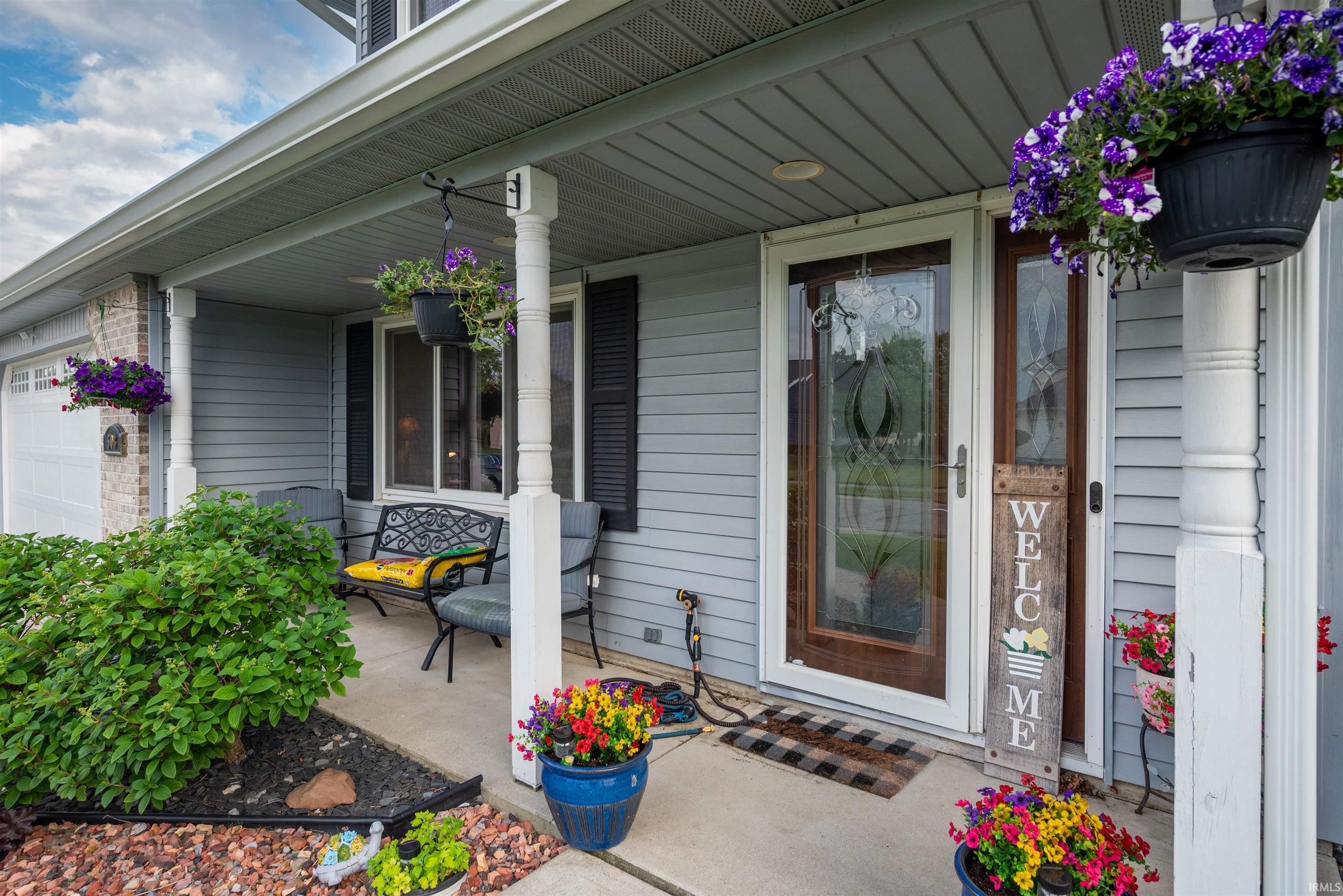 Covered front porch featuring gray siding, white trim, and a decorative glass entry door with a storm door