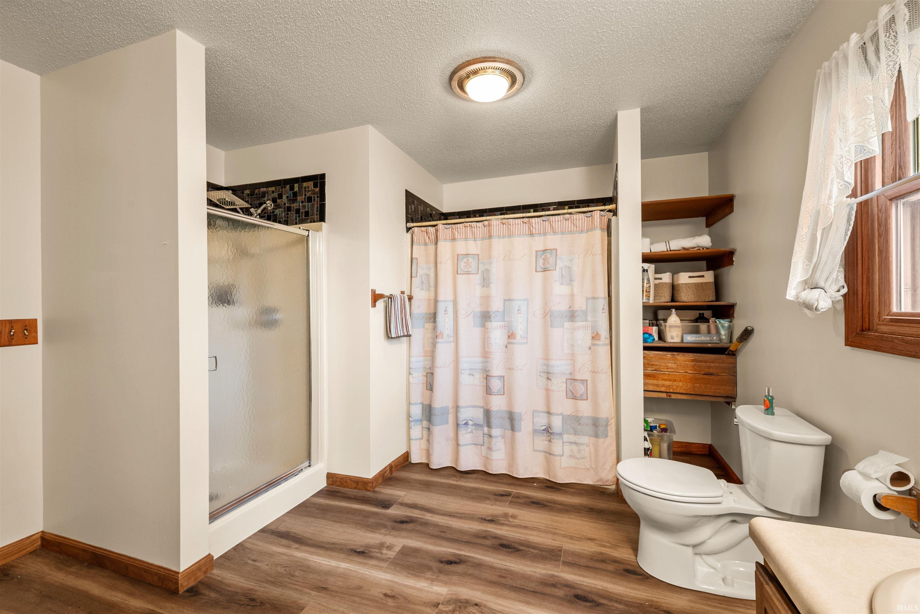 Bathroom featuring wood-finish flooring, a glass-enclosed shower, a separate tub/shower combination with privacy curtain, a window with wood trim, and built-in shelving