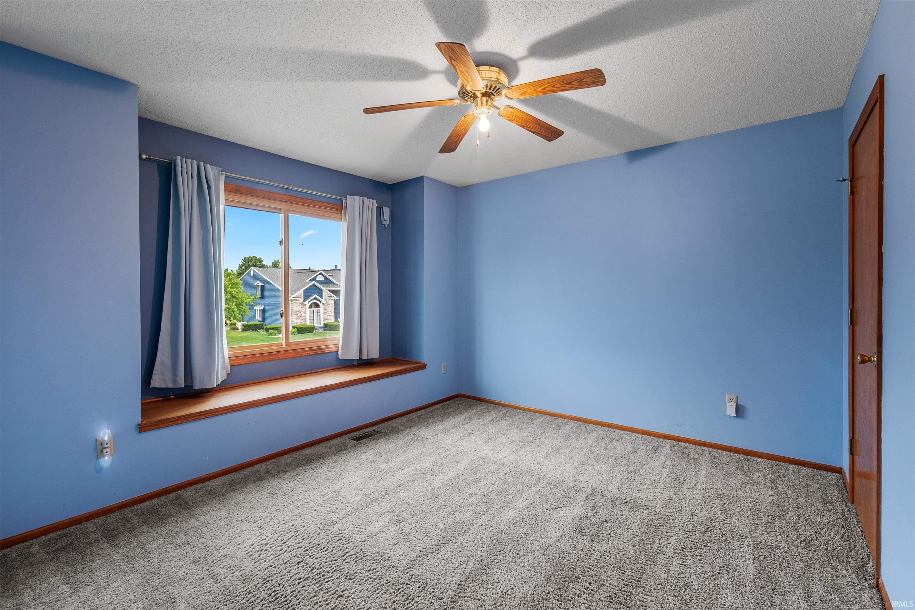 Carpeted room featuring a ceiling fan with integrated lighting, a window with a wood-finish sill, and a wood-finish door
