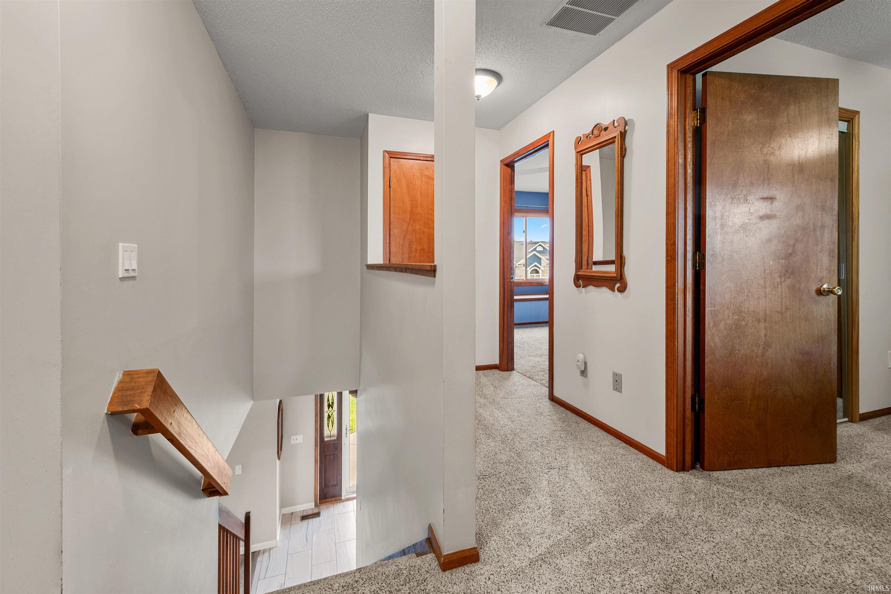 Upper-level hallway featuring light gray carpet flooring and wooden trim throughout