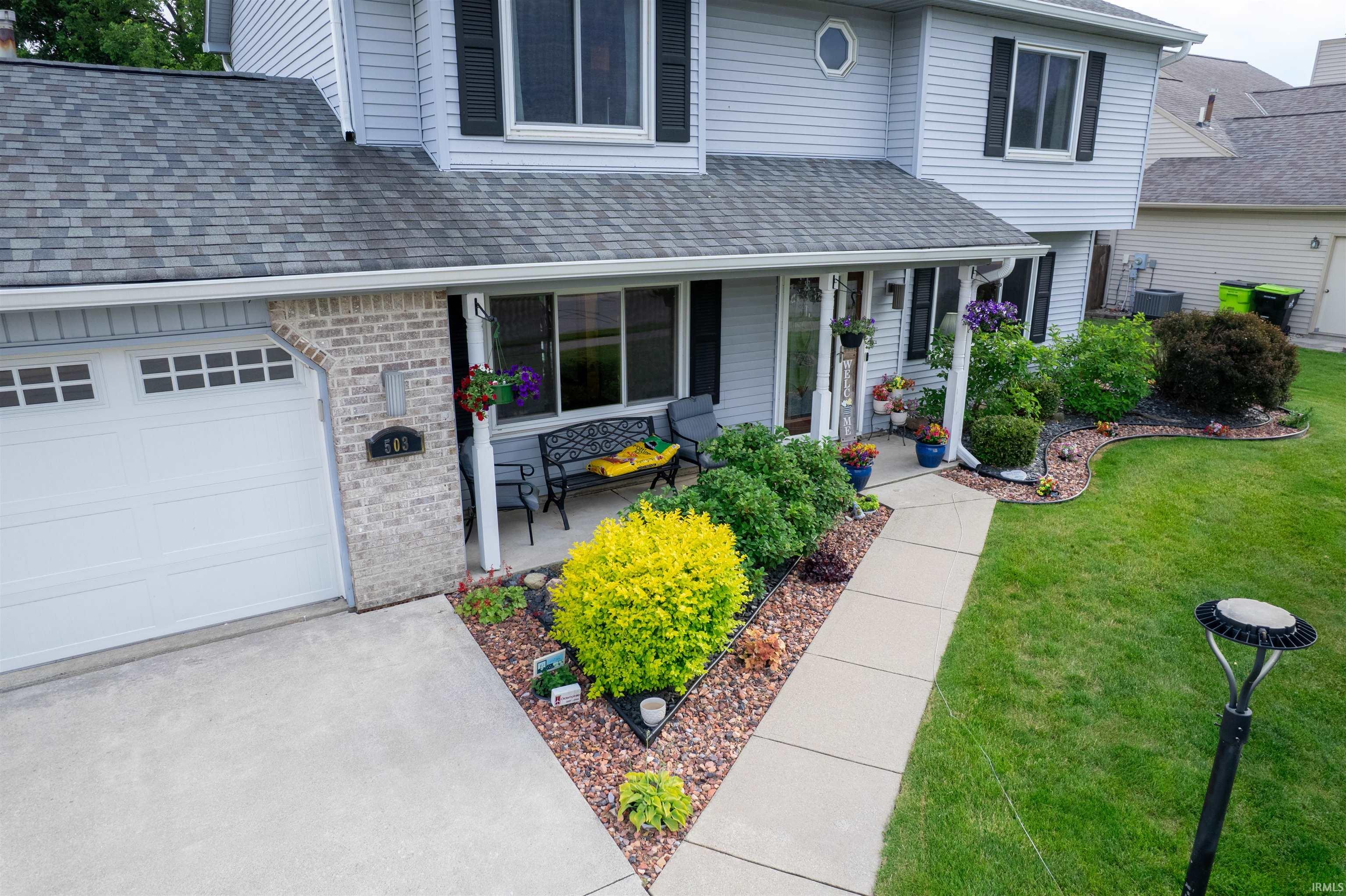 Traditional two-story residence featuring light gray siding, a covered front porch, and an attached garage with an overhead door