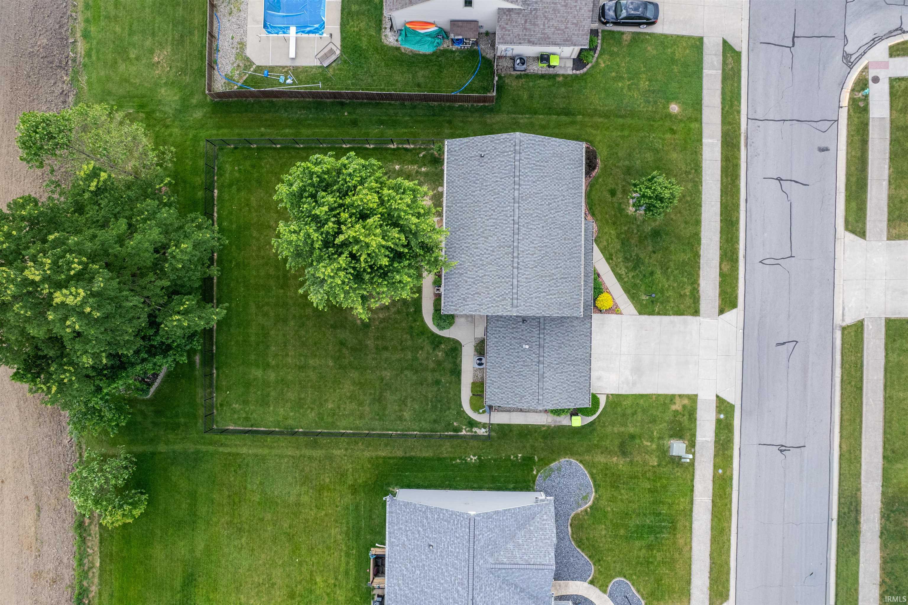 Residential property with a gray shingle roof, extensive green lawn, mature trees, and concrete driveway leading to a paved street