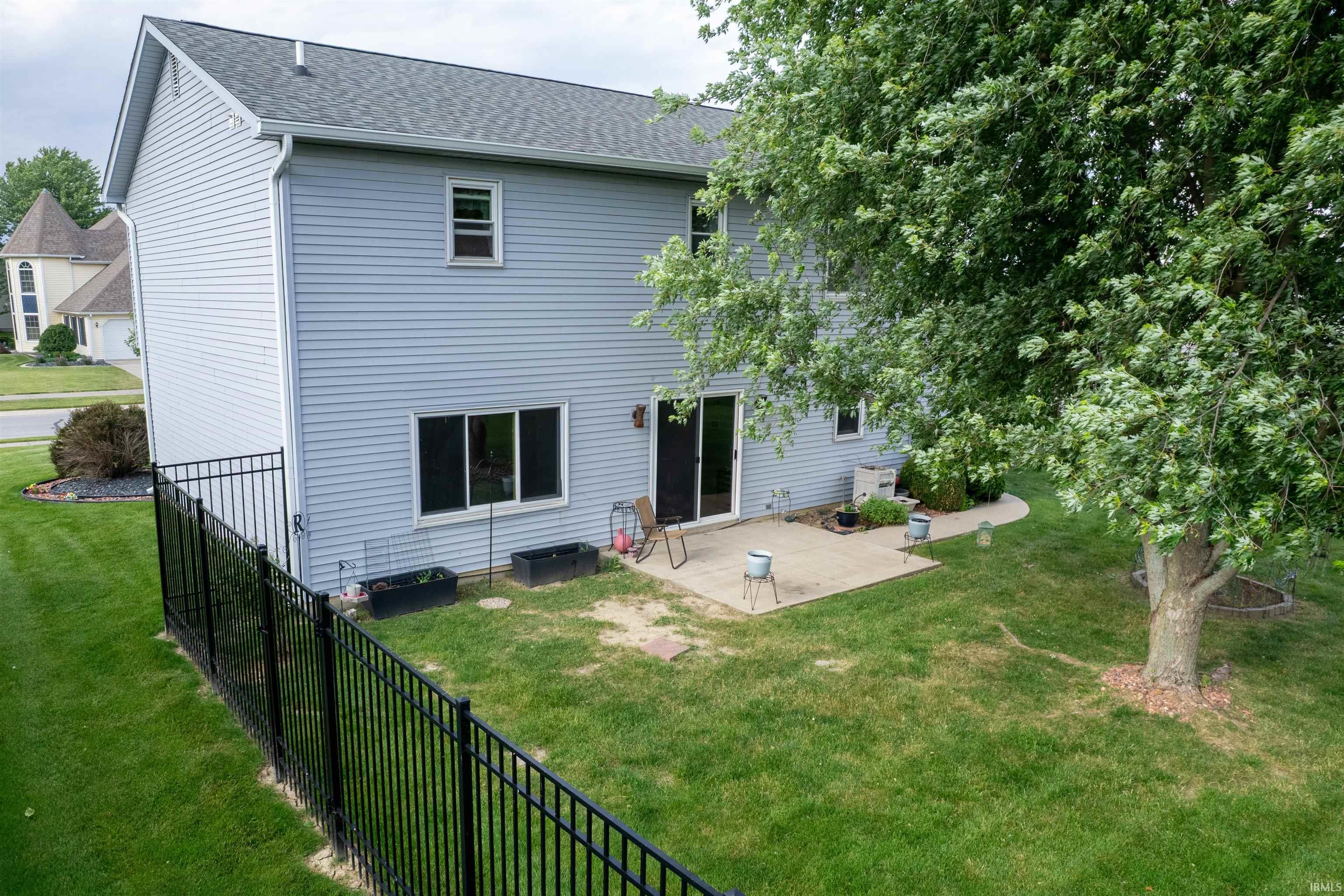 Expansive backyard featuring a manicured lawn, established shade tree, and a concrete patio