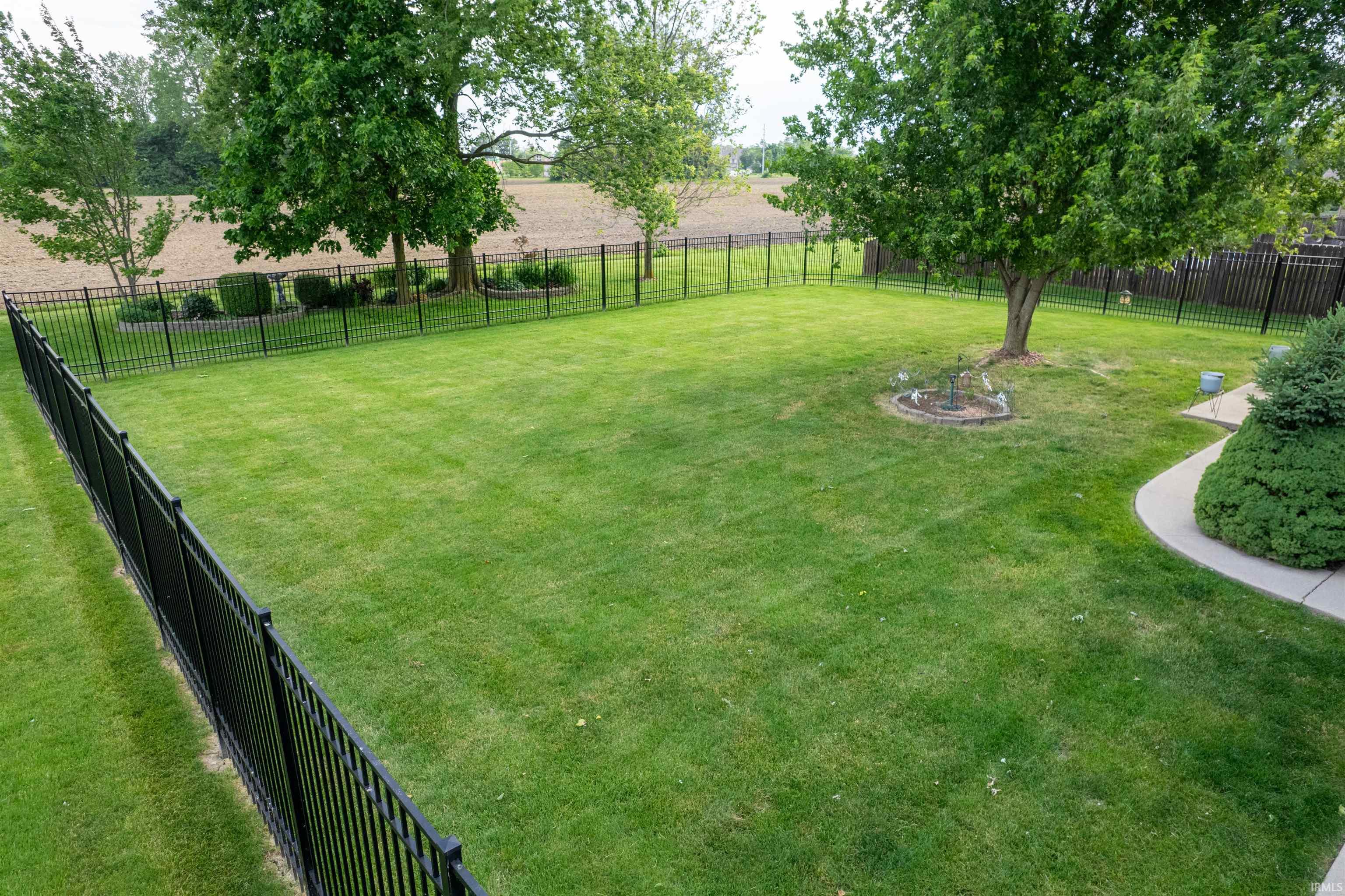 Expansive fenced backyard featuring a manicured lawn, established trees, and perimeter landscaping