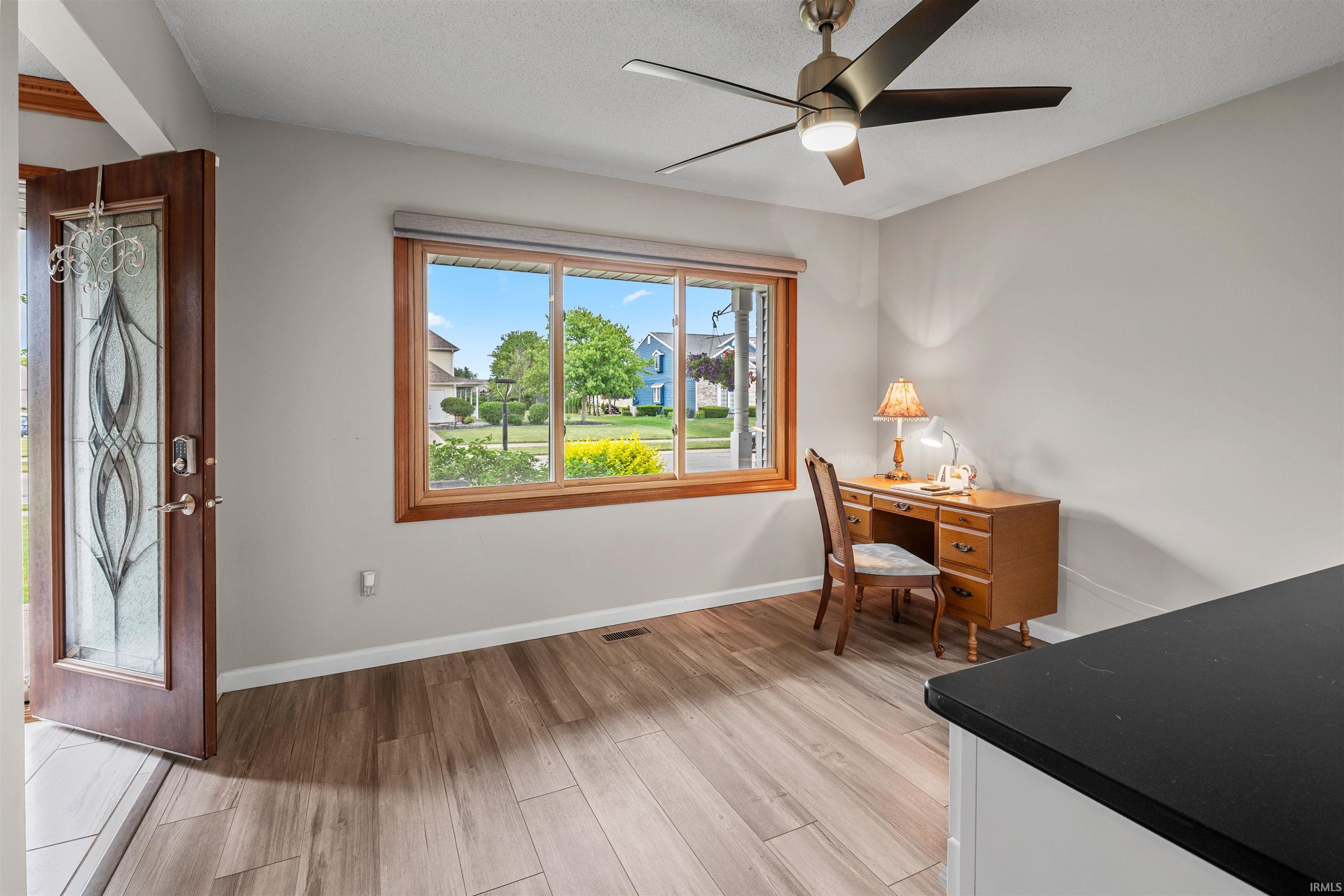 Entryway featuring a wood-finish door with decorative glass, wood-finish flooring, a ceiling fan with integrated lighting, a large window with wood trim, and light-colored walls