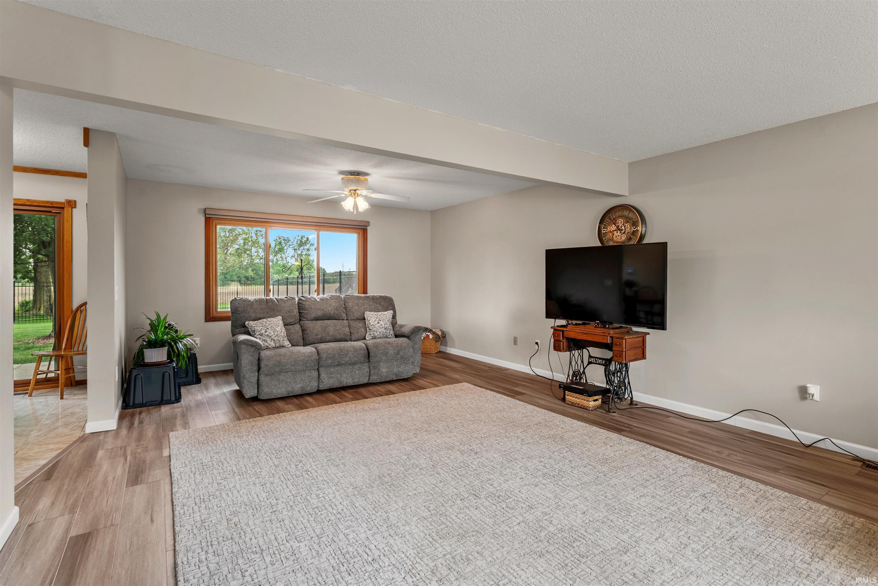 Spacious living area featuring wood-finish flooring, neutral wall tones, and a ceiling fan with integrated lighting