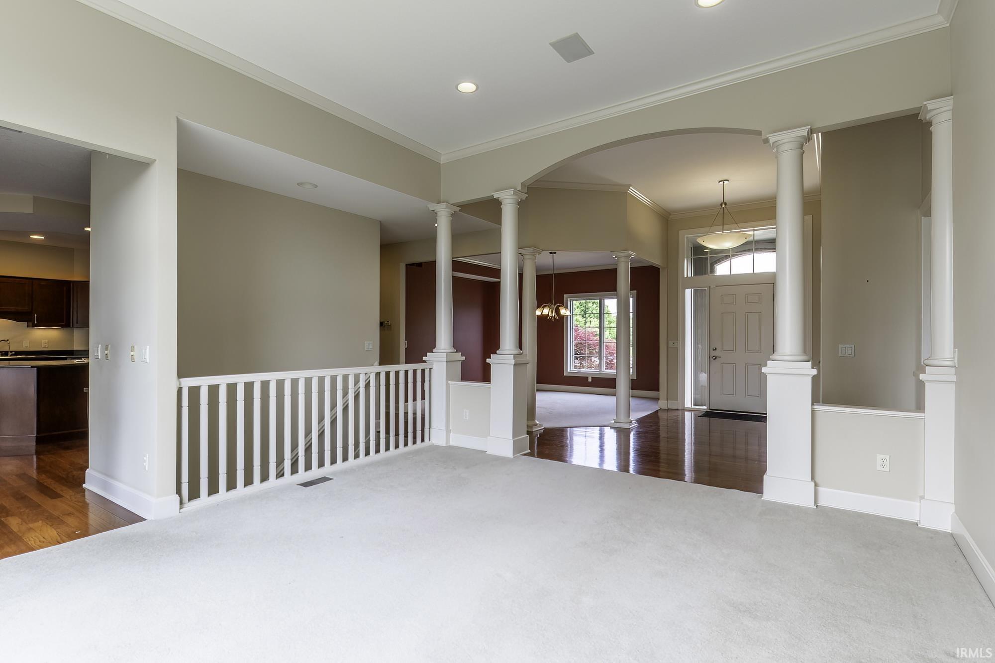 Foyer entrance featuring hardwood flooring, decorative columns, arched entryway, and a white paneled door with sidelights and transom window