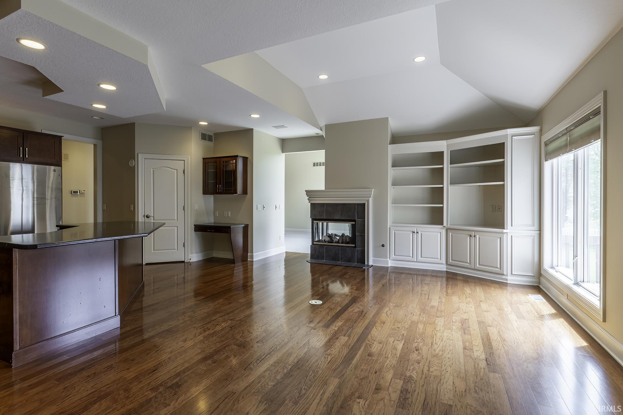 Open-concept living area featuring rich wood-finish flooring, a contemporary fireplace with a dark tile surround, and custom built-in shelving with lower cabinetry