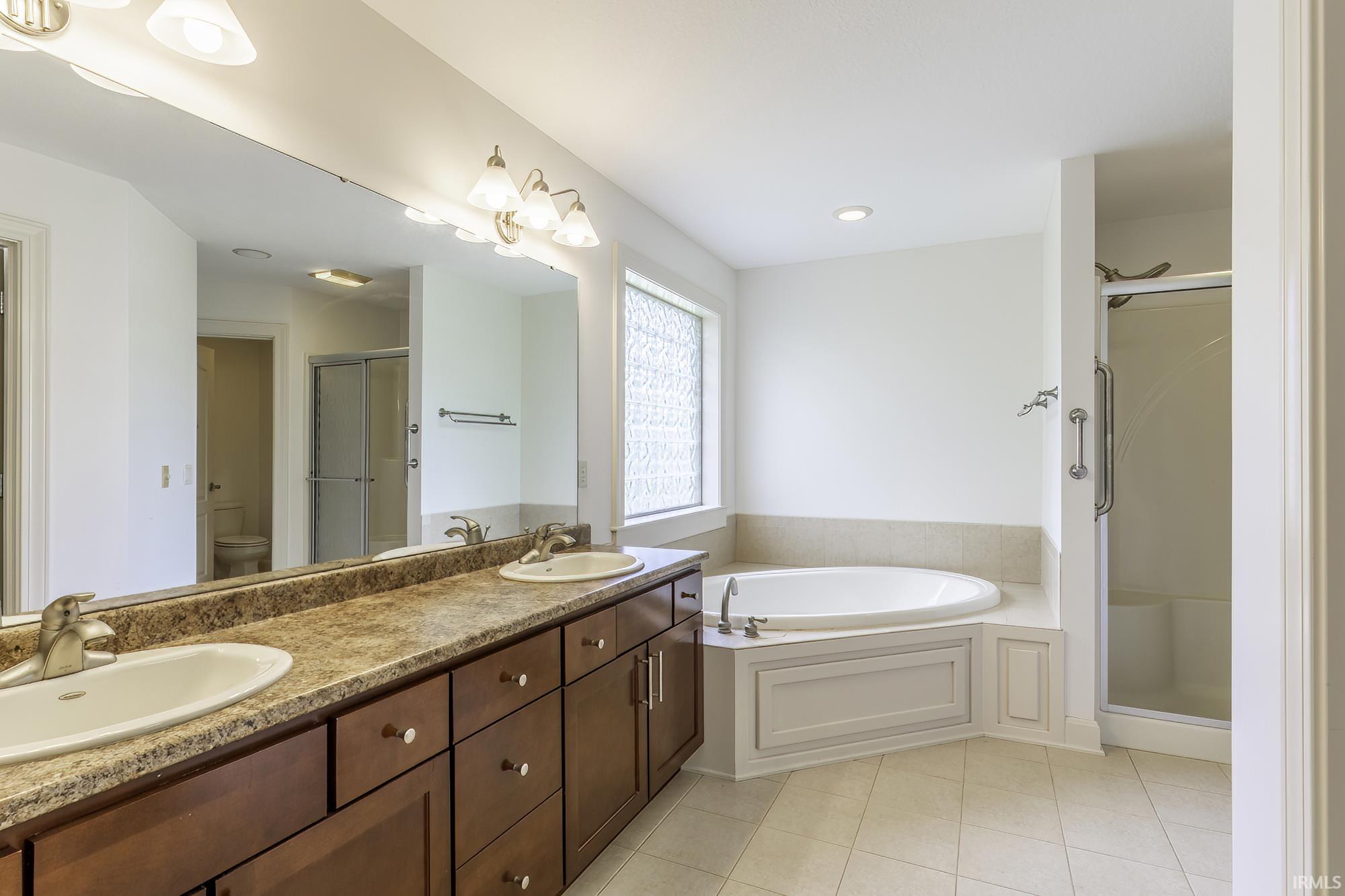 Expansive bathroom featuring a dual vanity with a stone-finish countertop, a large soaking tub, a separate glass-enclosed shower, and a privacy window with textured glass
