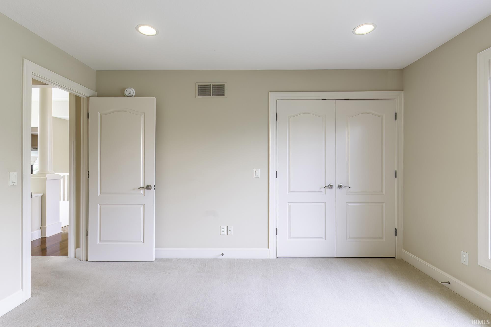 Spacious room featuring neutral wall tones, recessed lighting, double panel doors, and light-colored carpeting