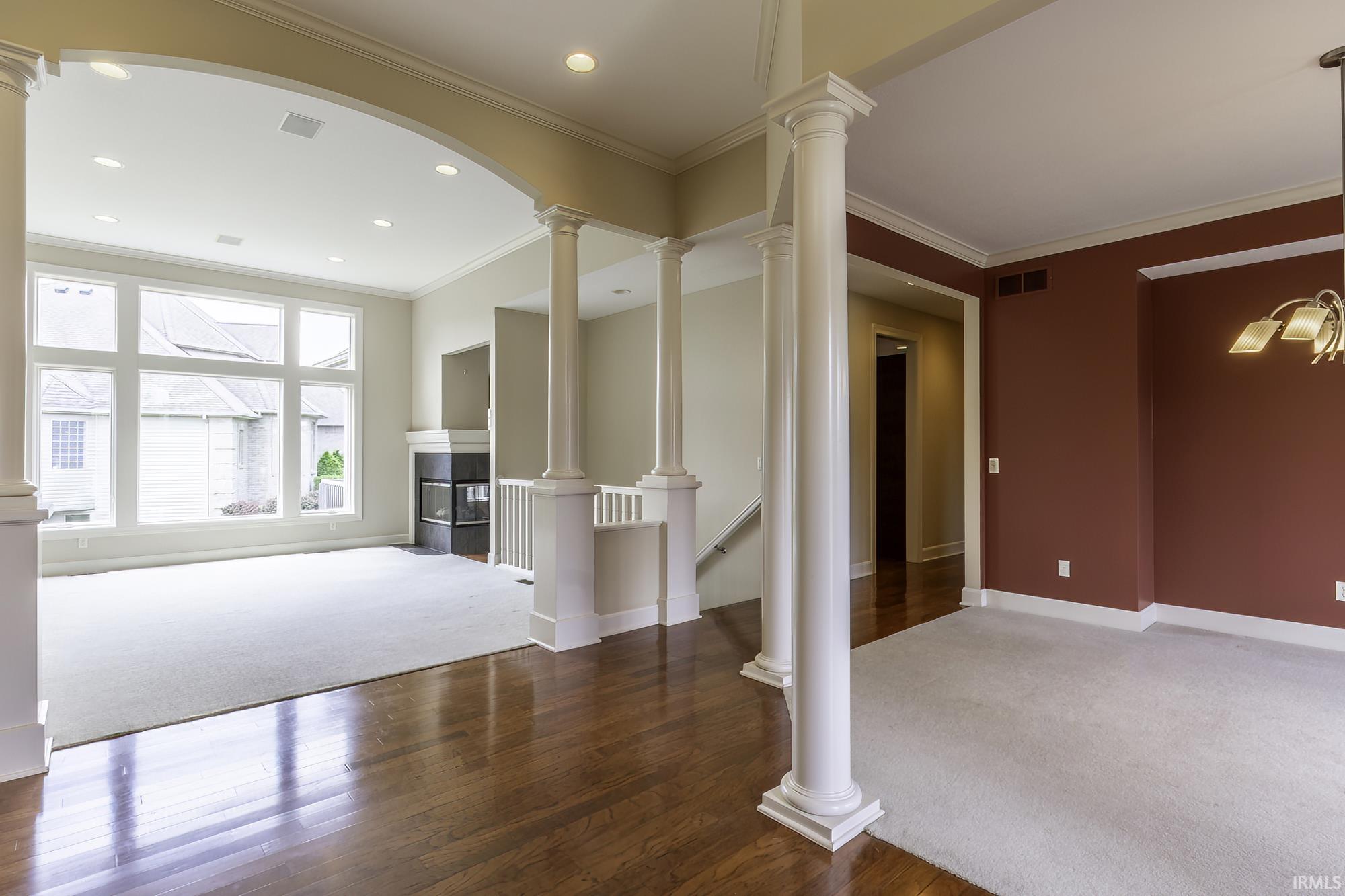 Archway entry with decorative columns, wood-finish flooring, recessed lighting, and a fireplace with a black surround
