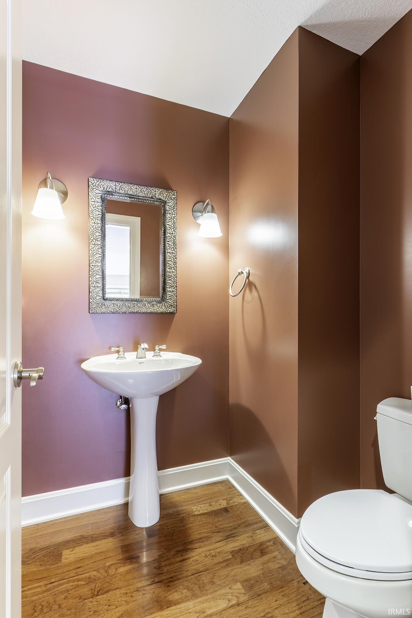 Powder room featuring a pedestal sink with a chrome faucet, a rectangular mirror, sconce lighting, and wood-finish flooring