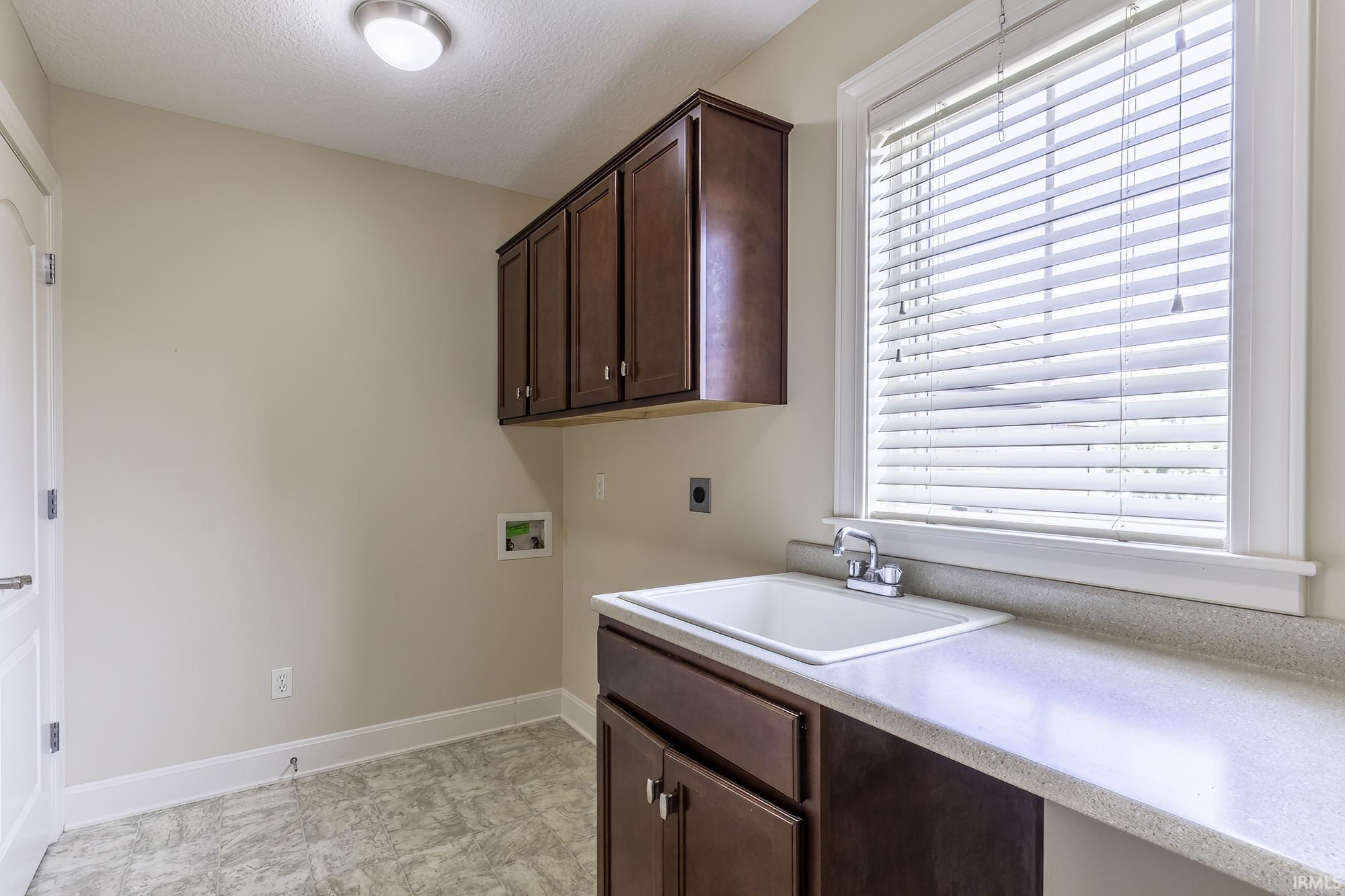 Laundry area featuring a utility sink with a chrome faucet, dark wood-finish cabinetry, and a light-toned countertop