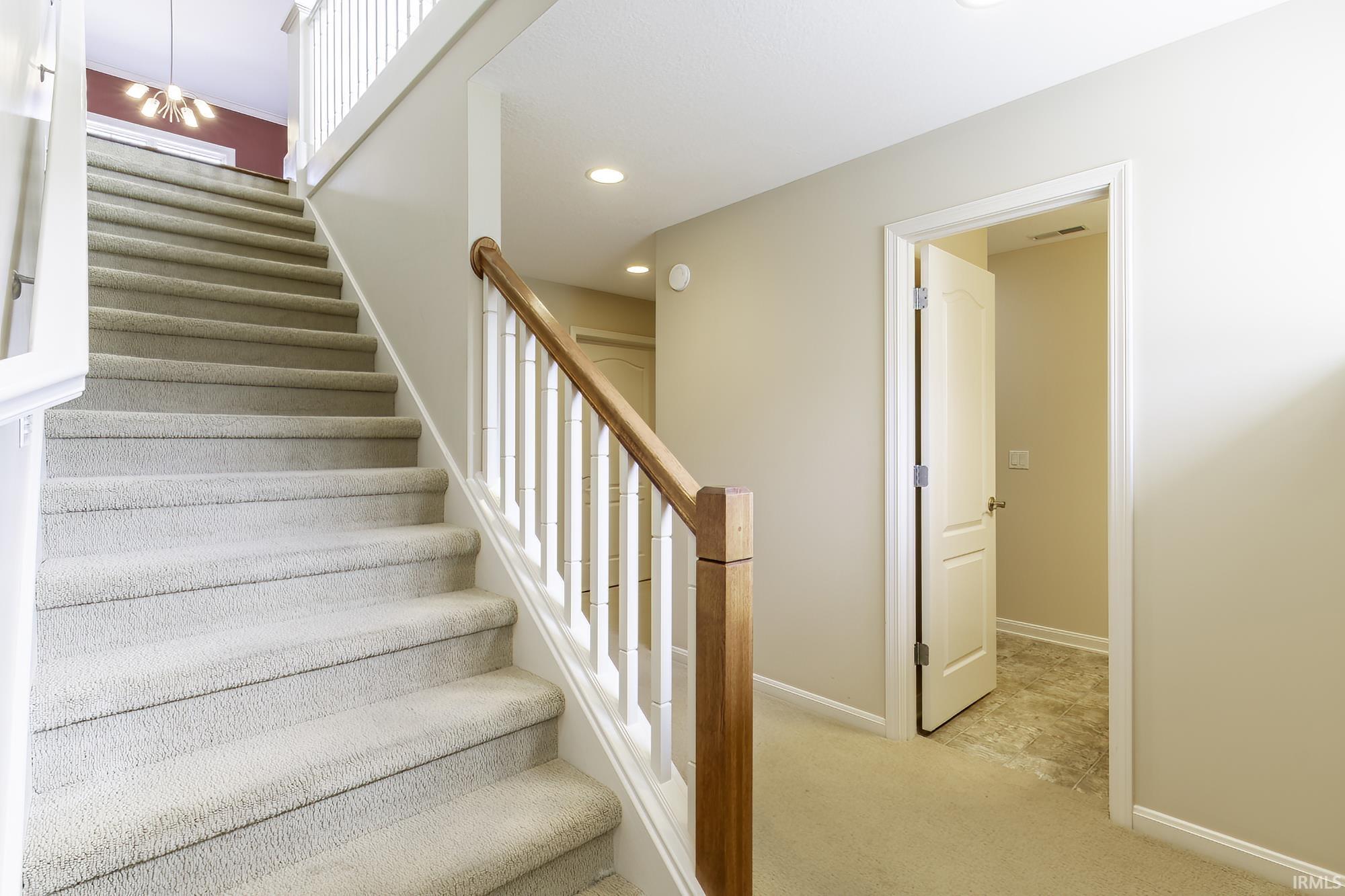 Carpeted staircase with white risers and a wood-finish handrail, complemented by white balusters