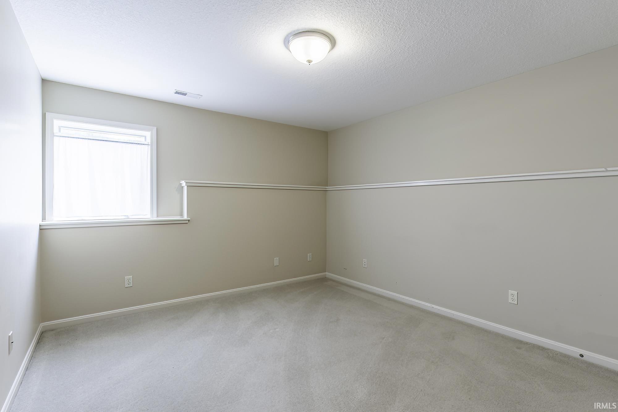 Carpeted interior space featuring a window with white trim, a flush-mount ceiling light, white baseboards, and chair rail molding