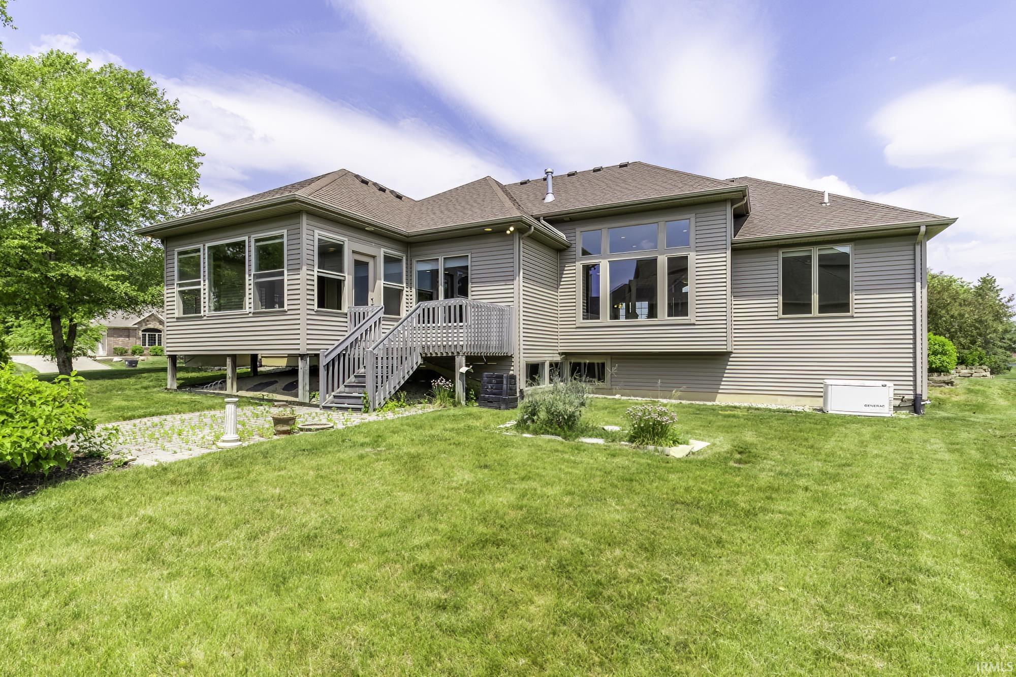 Rear exterior featuring beige siding, multiple windows, and a multi-level deck with stairs descending to a green lawn