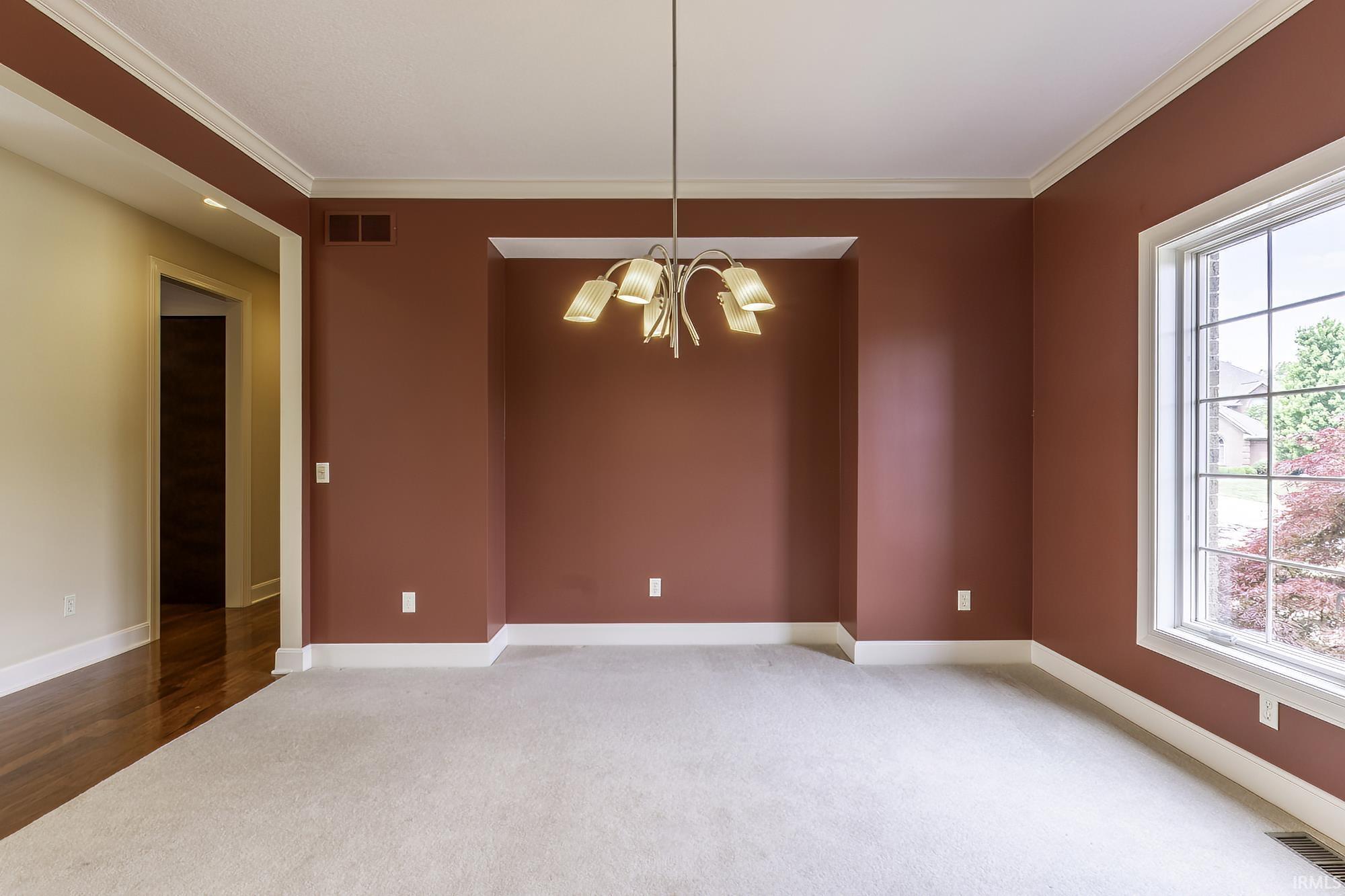 Spacious room featuring carpeting, a prominent window with grid panes, crown molding, and a built-in wall niche
