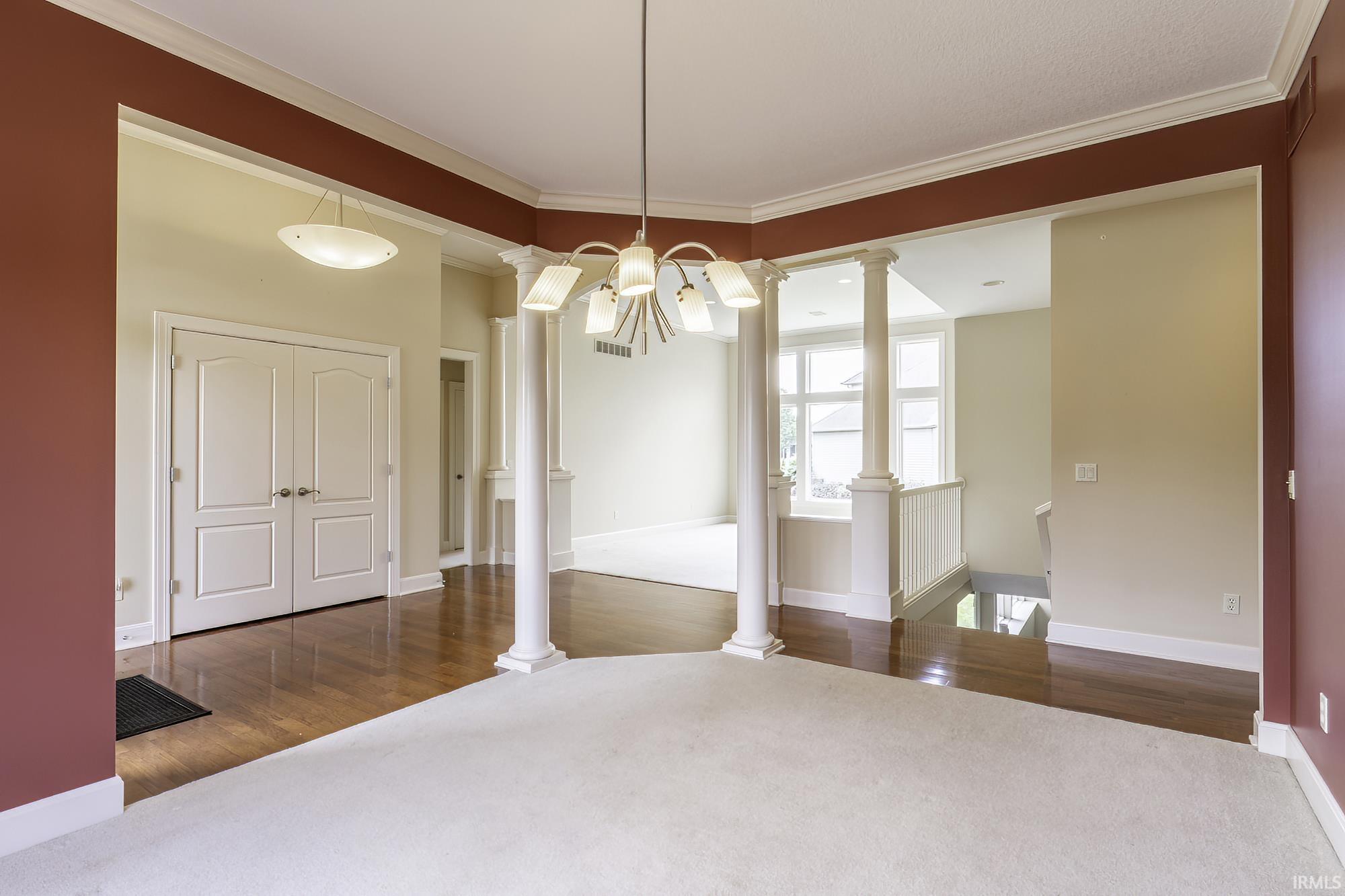Interior space featuring a carpeted foreground, a tiered chandelier, and a hallway entrance with double panel doors
