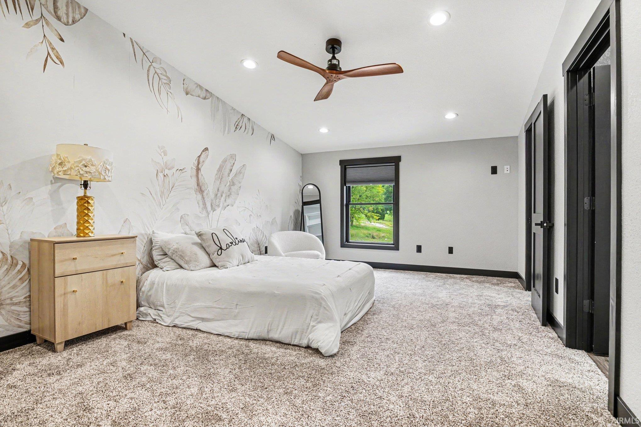 Spacious room featuring textured carpet flooring, a decorative accent wall, a ceiling fan with light, recessed lighting, and a window with a black frame