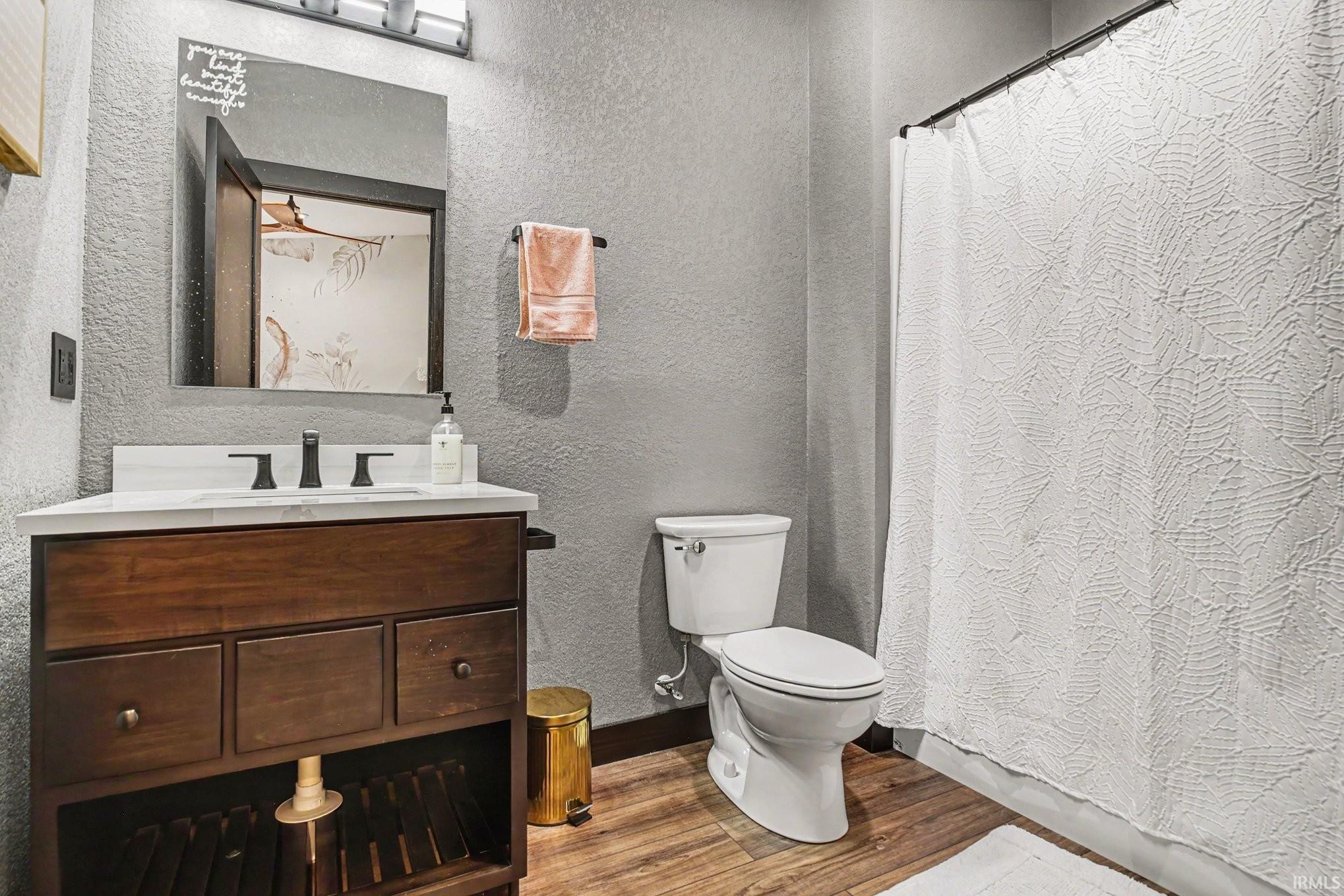 Bathroom featuring wood-finish flooring, a freestanding vanity with integrated sink, white countertop, and dark-toned fixtures