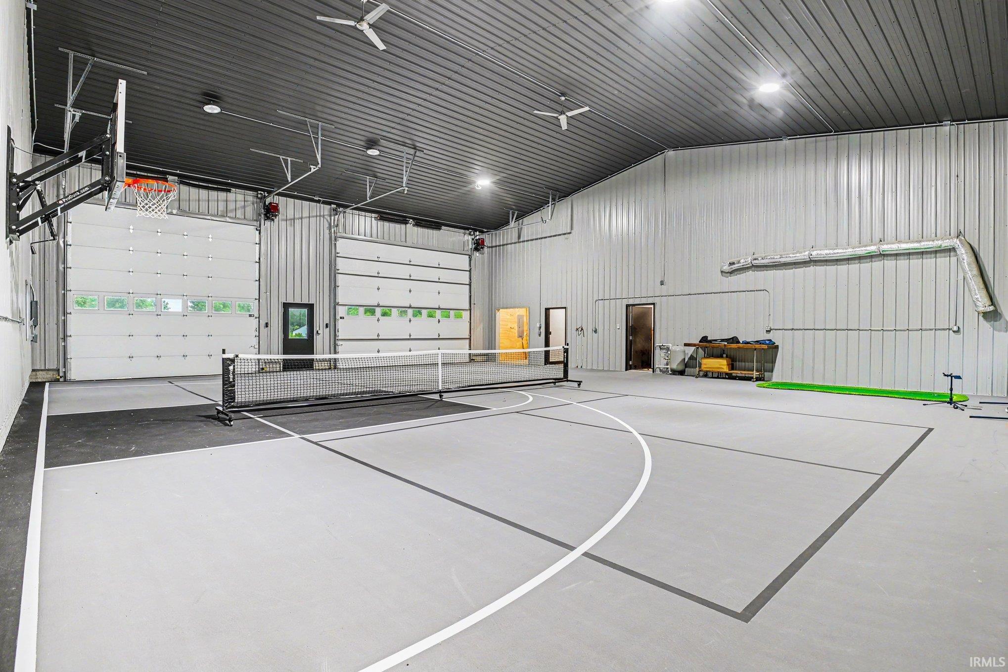 Spacious indoor court featuring a painted pickleball court, basketball hoop, and multiple overhead ceiling fans
