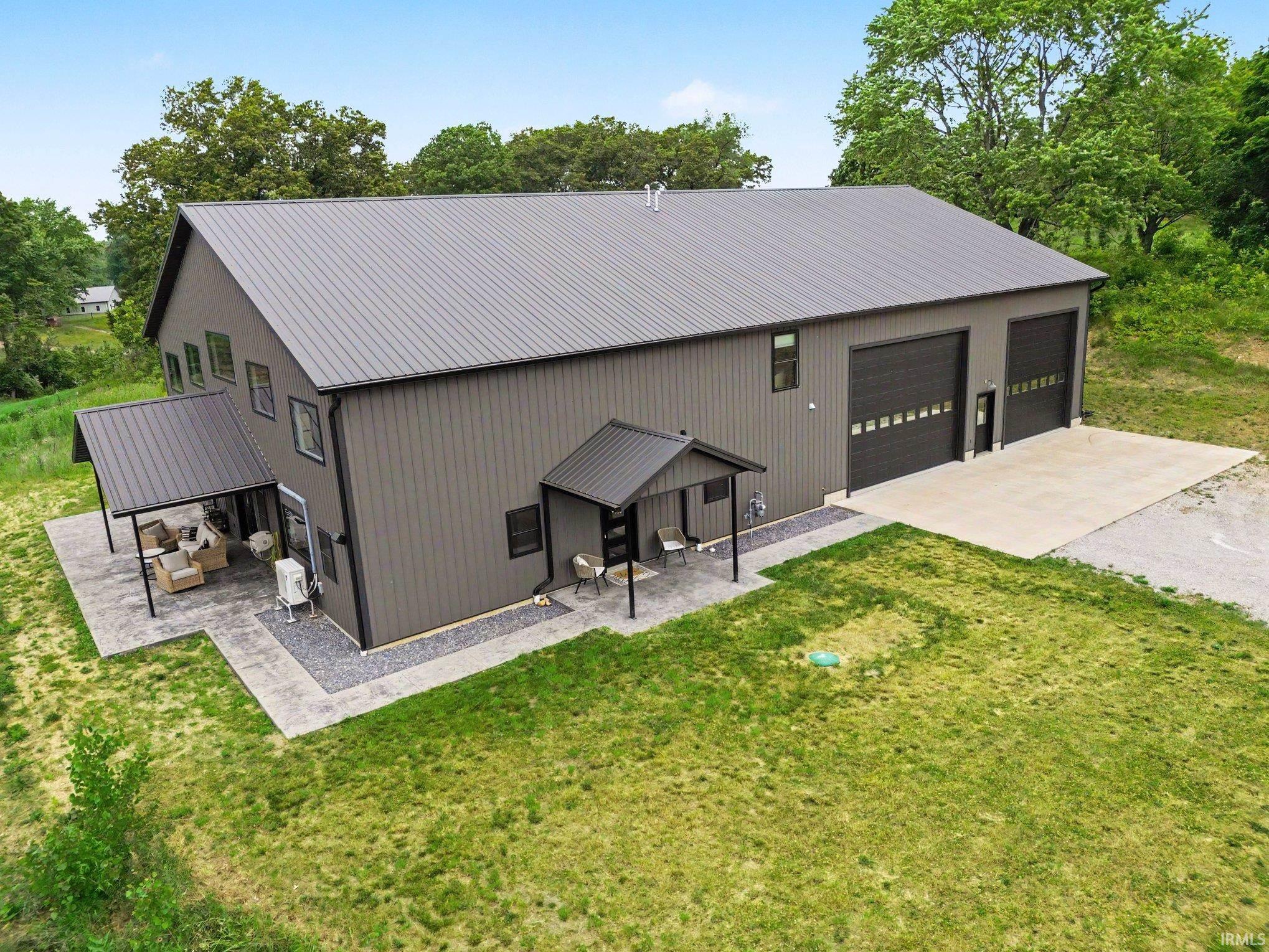 Modern gray metal building with two large garage doors, a concrete pad, and a covered patio with a paved surface