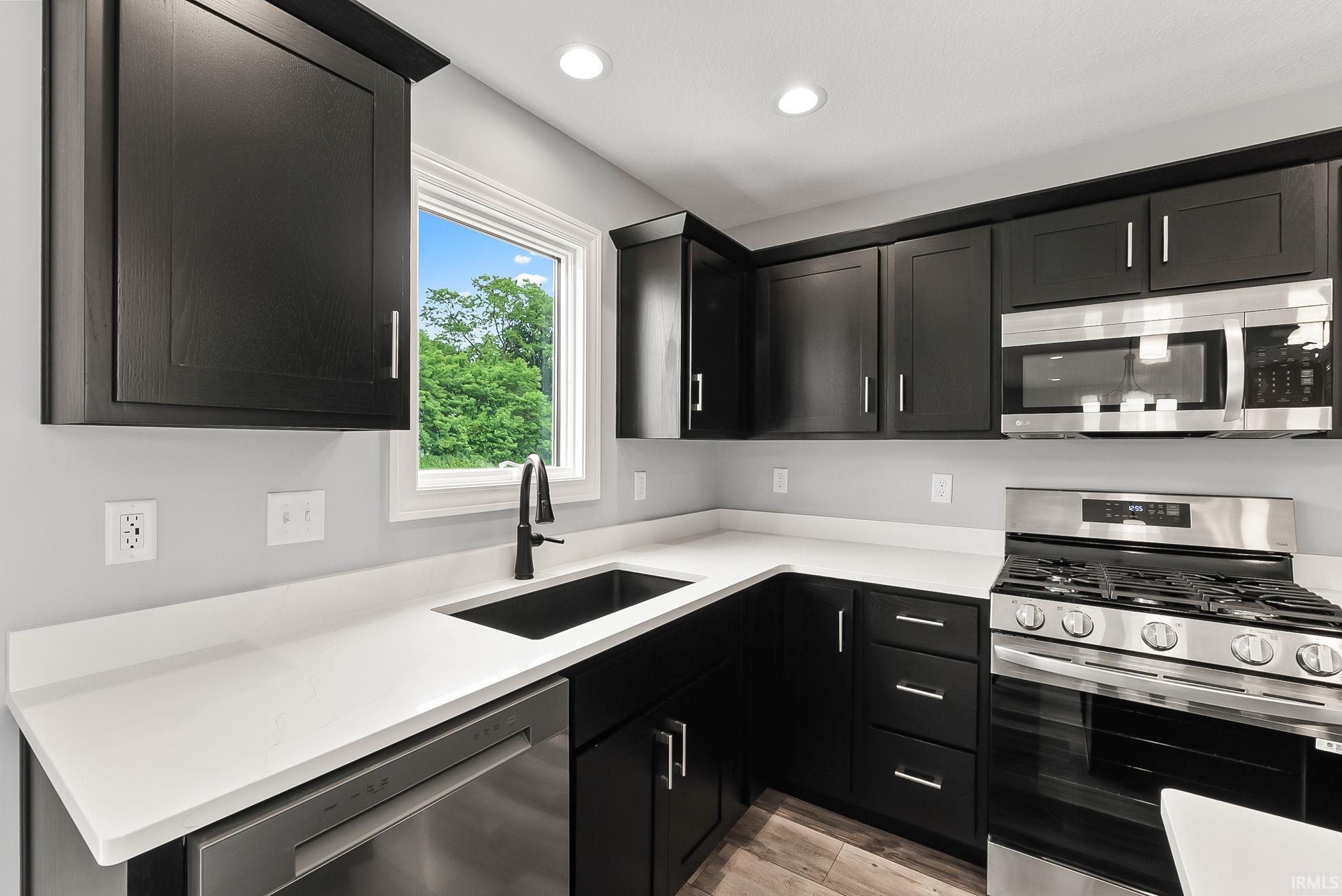Kitchen featuring dark cabinetry, light countertops, stainless steel appliances, a black undermount sink with a black faucet, and recessed lighting