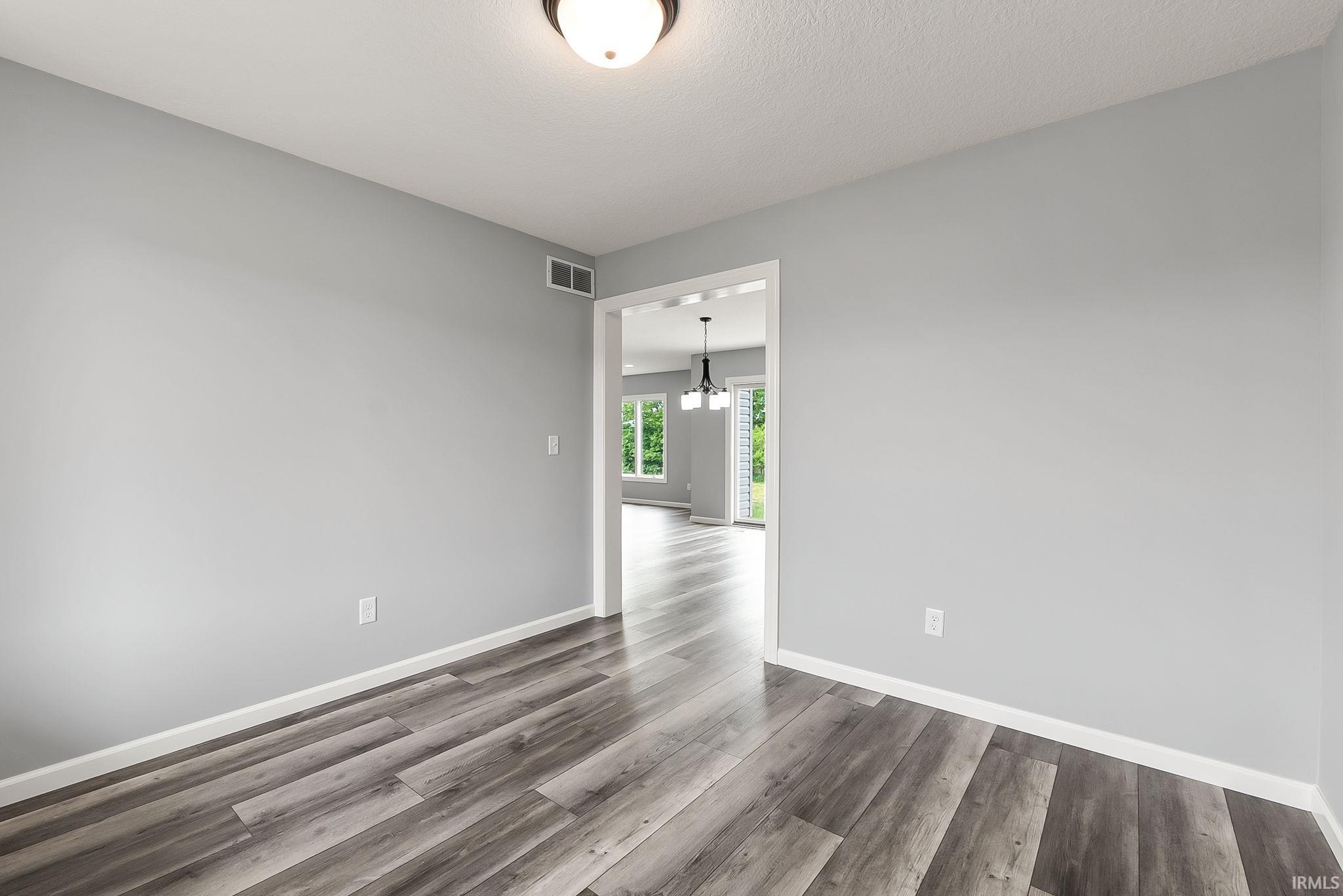 Spacious room featuring wood-finish flooring, light gray walls, white baseboards, and a semi-flush mount ceiling light