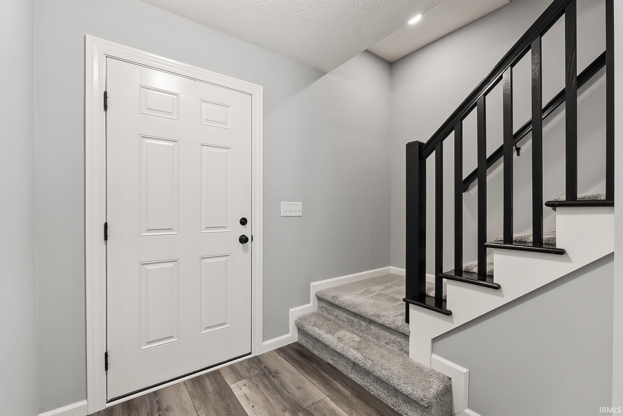 Entryway featuring a paneled door with black hardware, wood-finish flooring, and a carpeted staircase with a black balustrade
