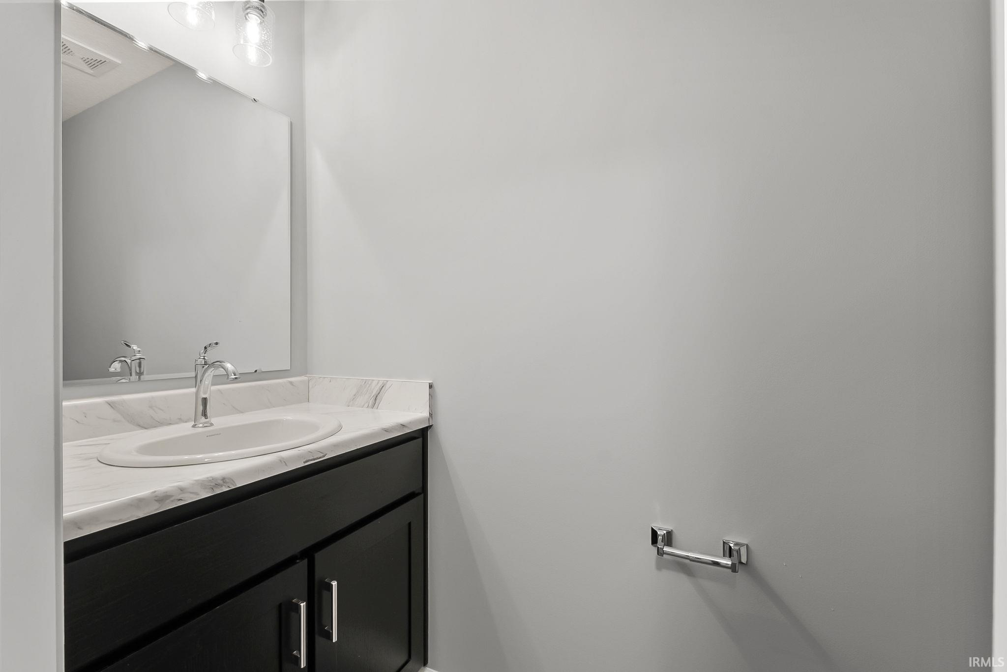 Bathroom vanity featuring dark cabinetry, a white countertop with subtle veining, an undermount sink, and a chrome faucet