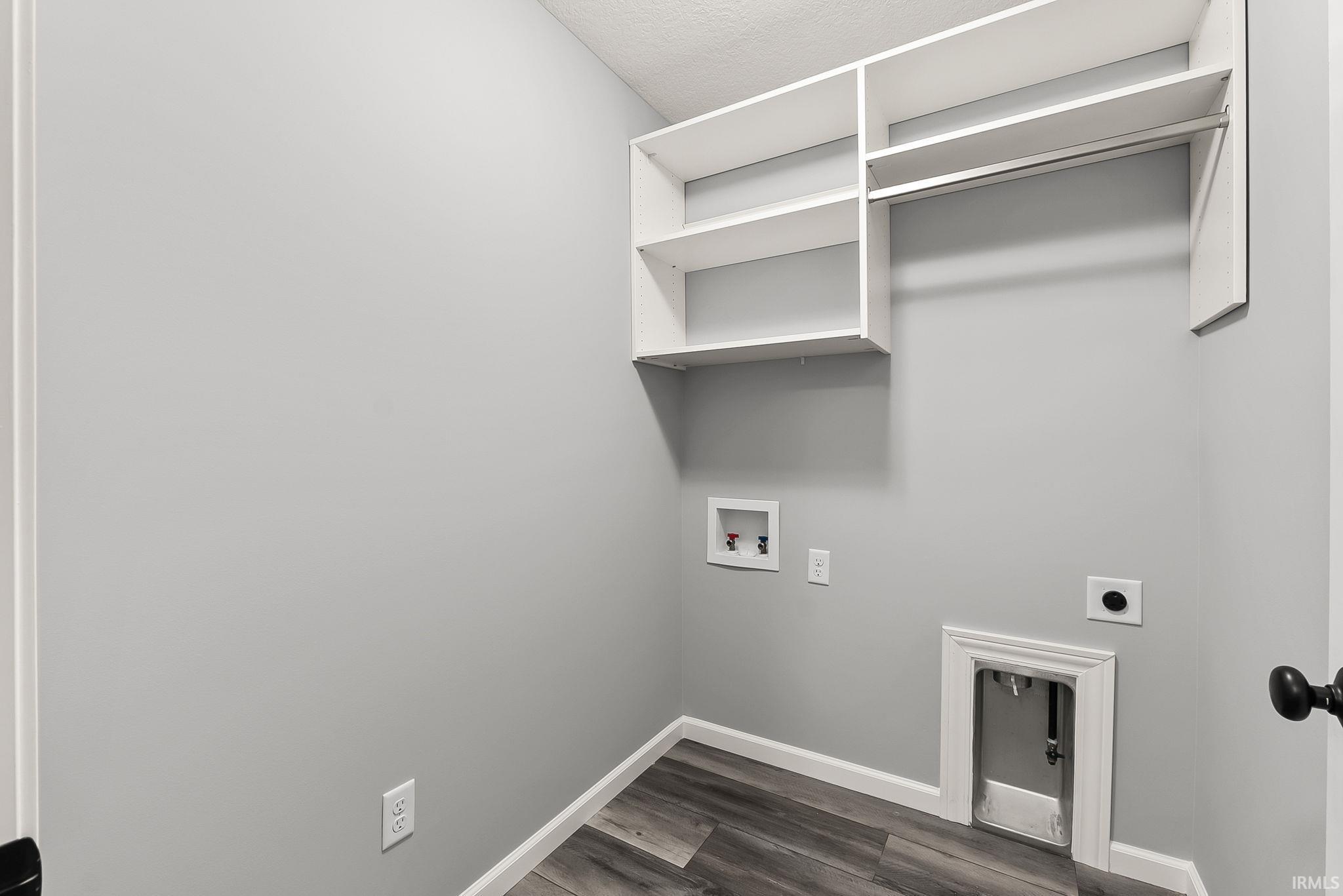 Dedicated laundry area featuring wood-finish flooring, light gray walls, built-in white shelving, and a hanging rod