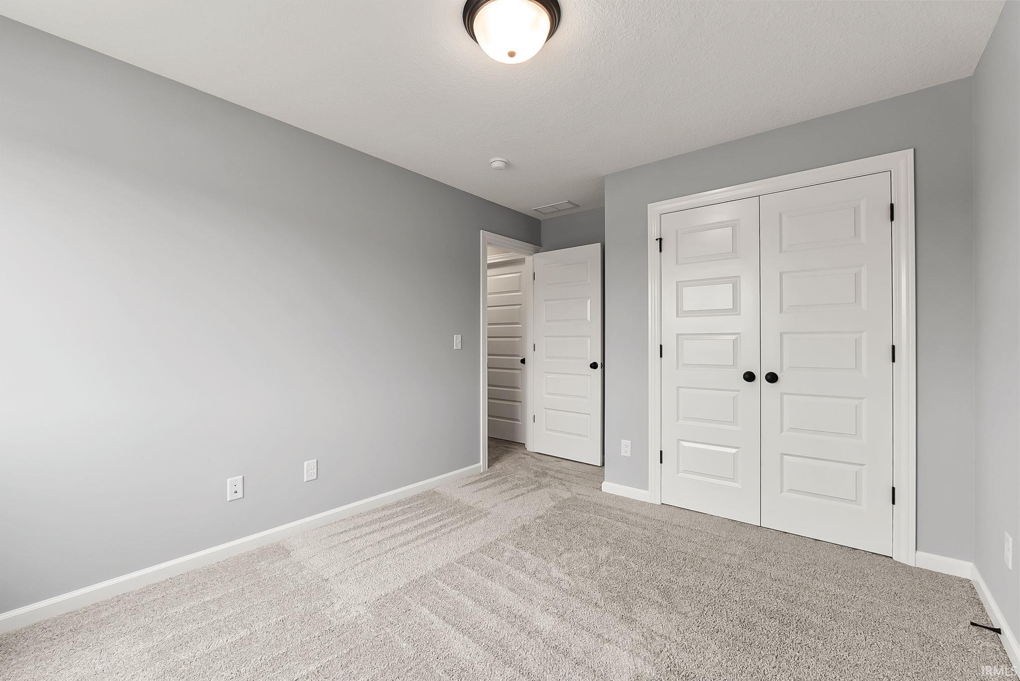 Spacious room featuring neutral gray walls and light-toned carpet flooring