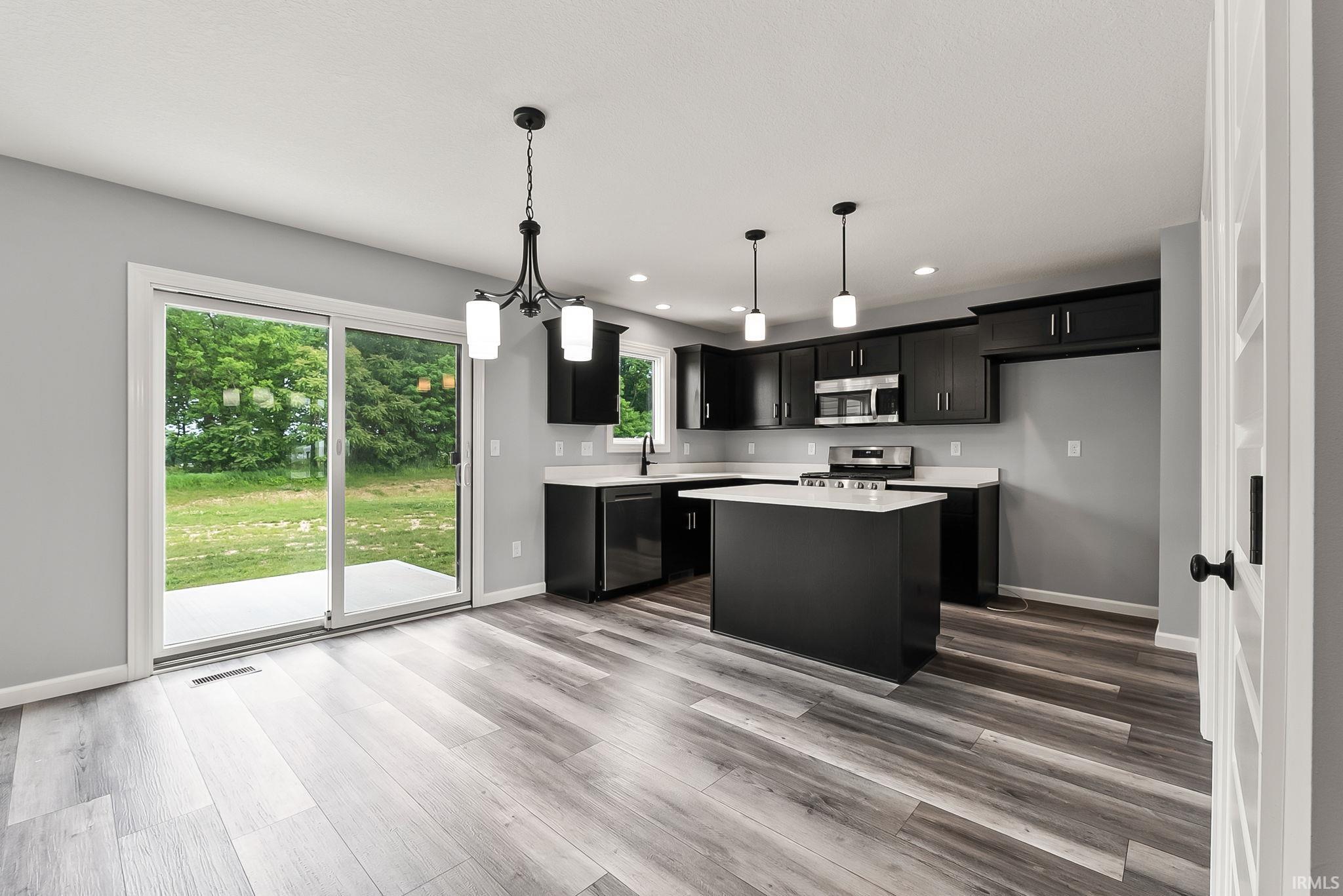 Open-concept kitchen and dining area featuring wood-finish flooring, dark cabinetry, light countertops, and stainless steel appliances
