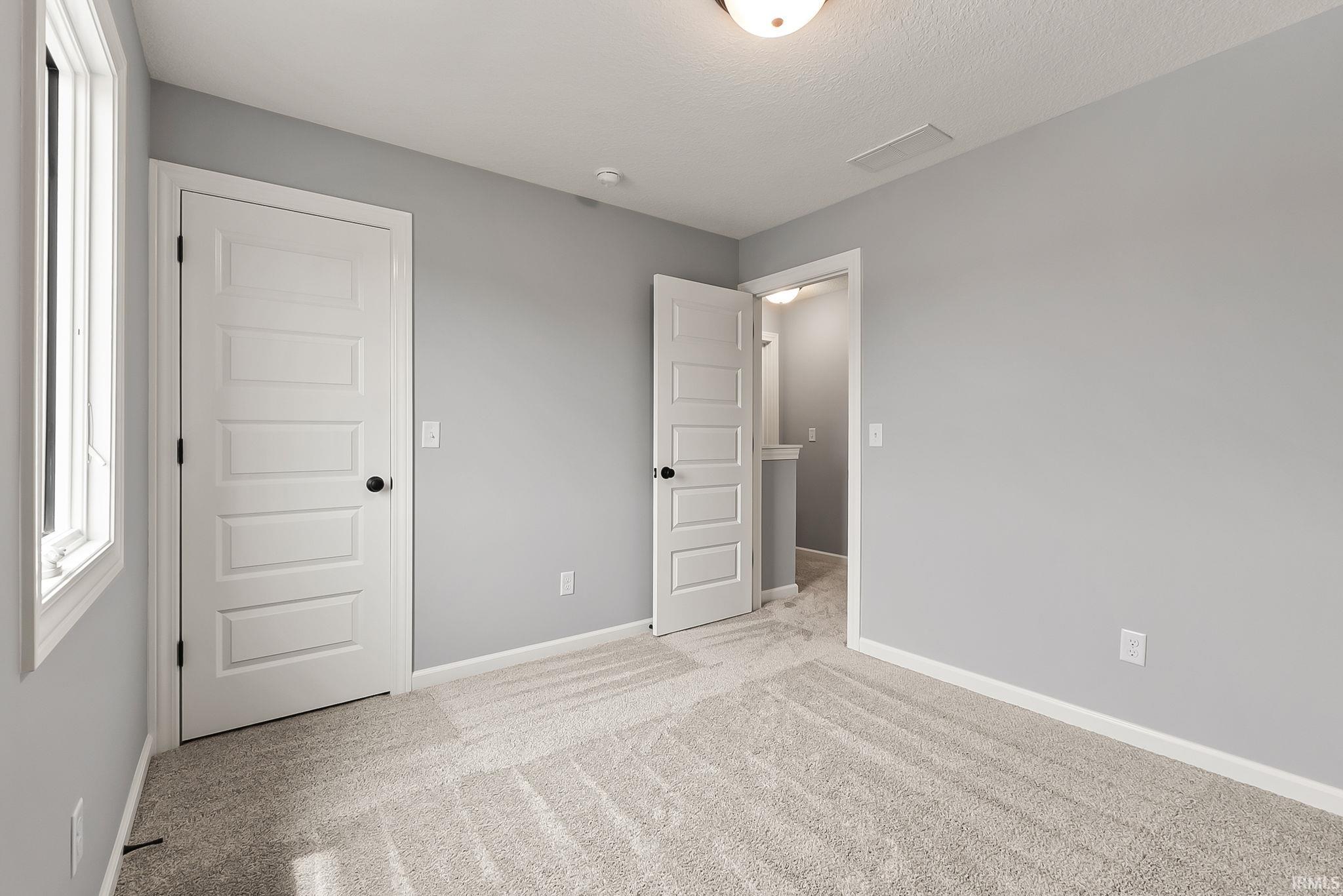 Neutral gray wall paint, light-colored carpeting, white trim, and a five-panel interior door with matte black hardware