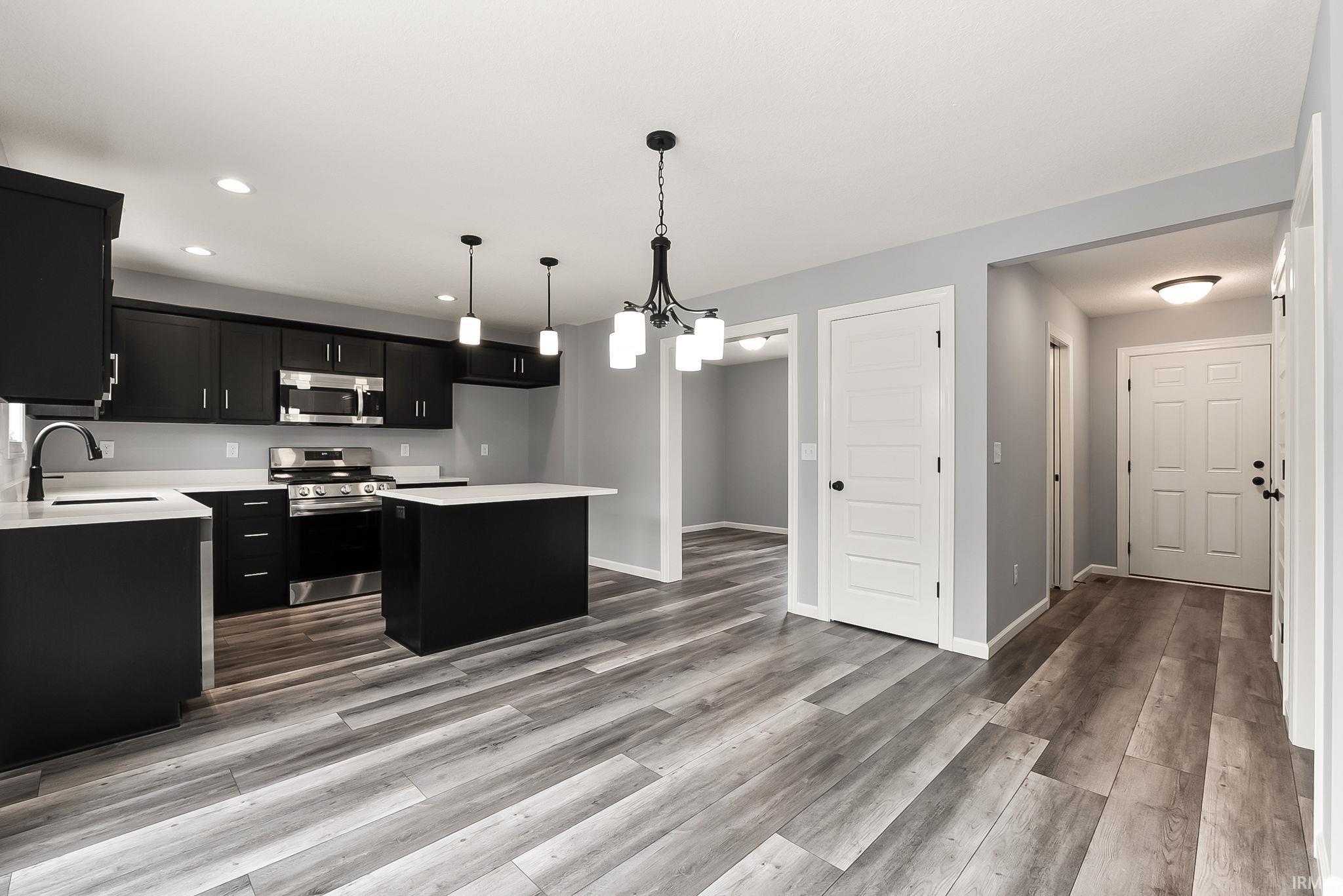 Open-concept living space featuring wood-finish flooring, a kitchen with black cabinetry and stainless steel appliances, a kitchen island with white countertop, and recessed lighting