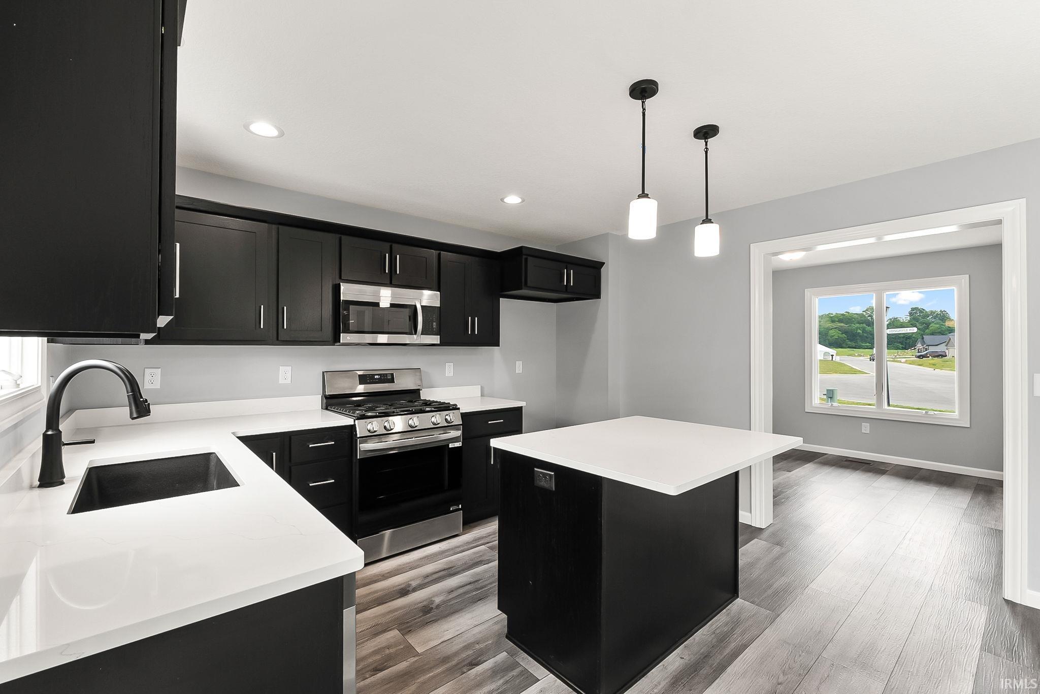 Modern kitchen featuring dark cabinetry, white countertops, stainless steel appliances, and wood-finish flooring