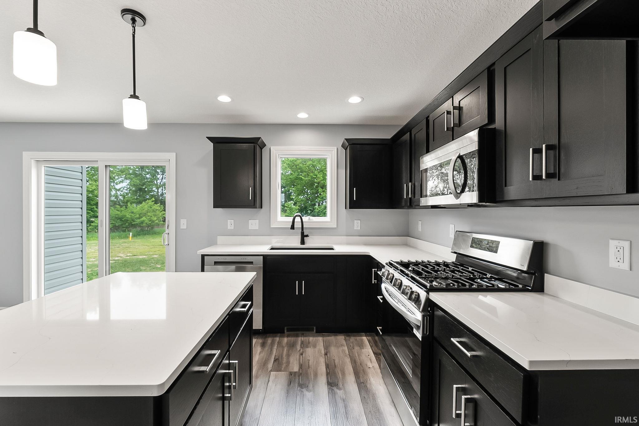 Modern kitchen featuring an island with a white countertop, dark wood-finish cabinetry, stainless steel appliances, and a gas range
