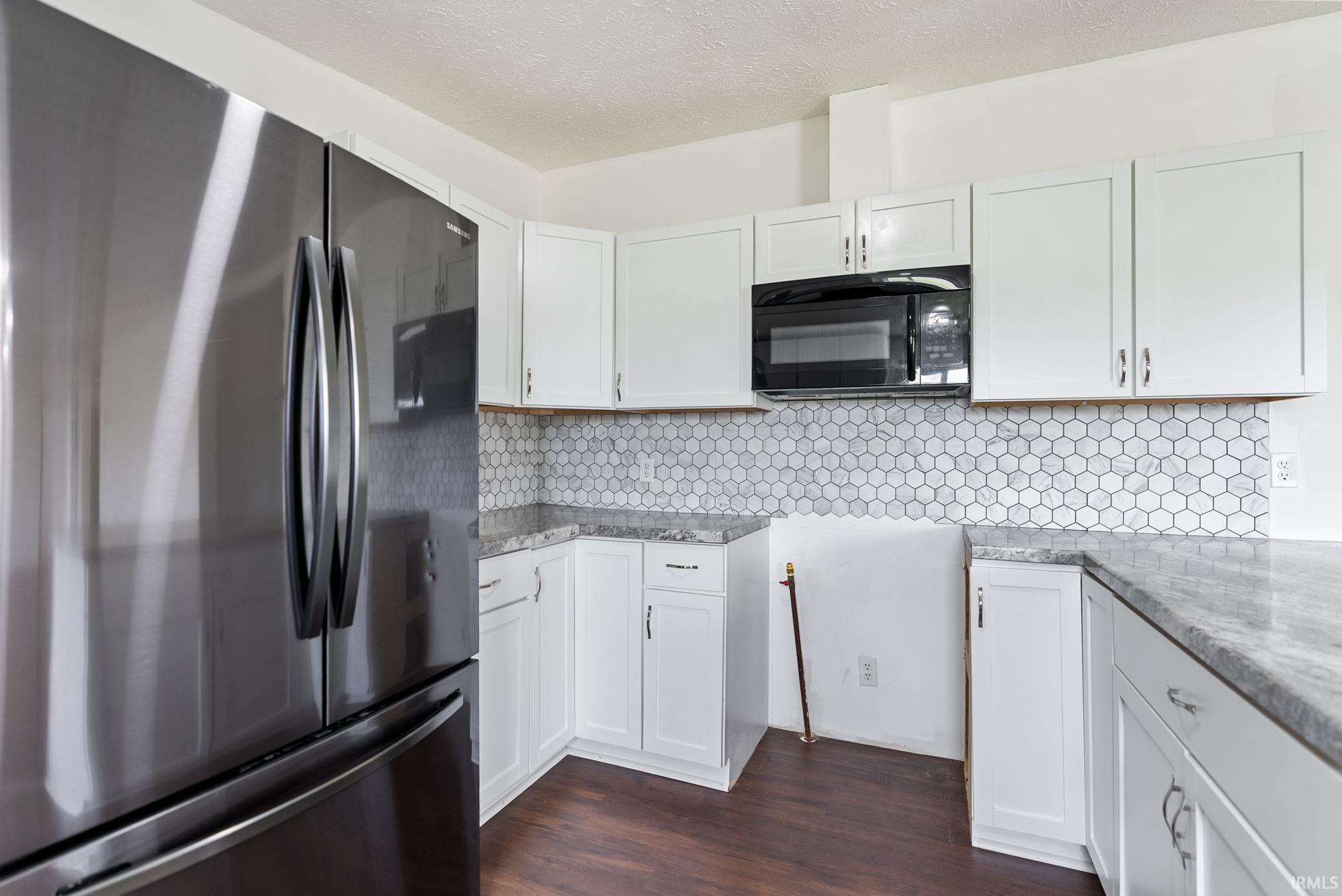 Stainless steel refrigerator paired with white cabinetry and dark wood-finish flooring
