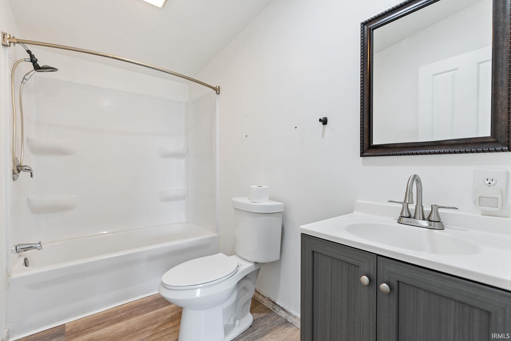 Bathroom featuring a white tub/shower combination with a curved shower rod, a toilet, a vanity with a white countertop, a dark gray wood-finish cabinet, and a framed mirror