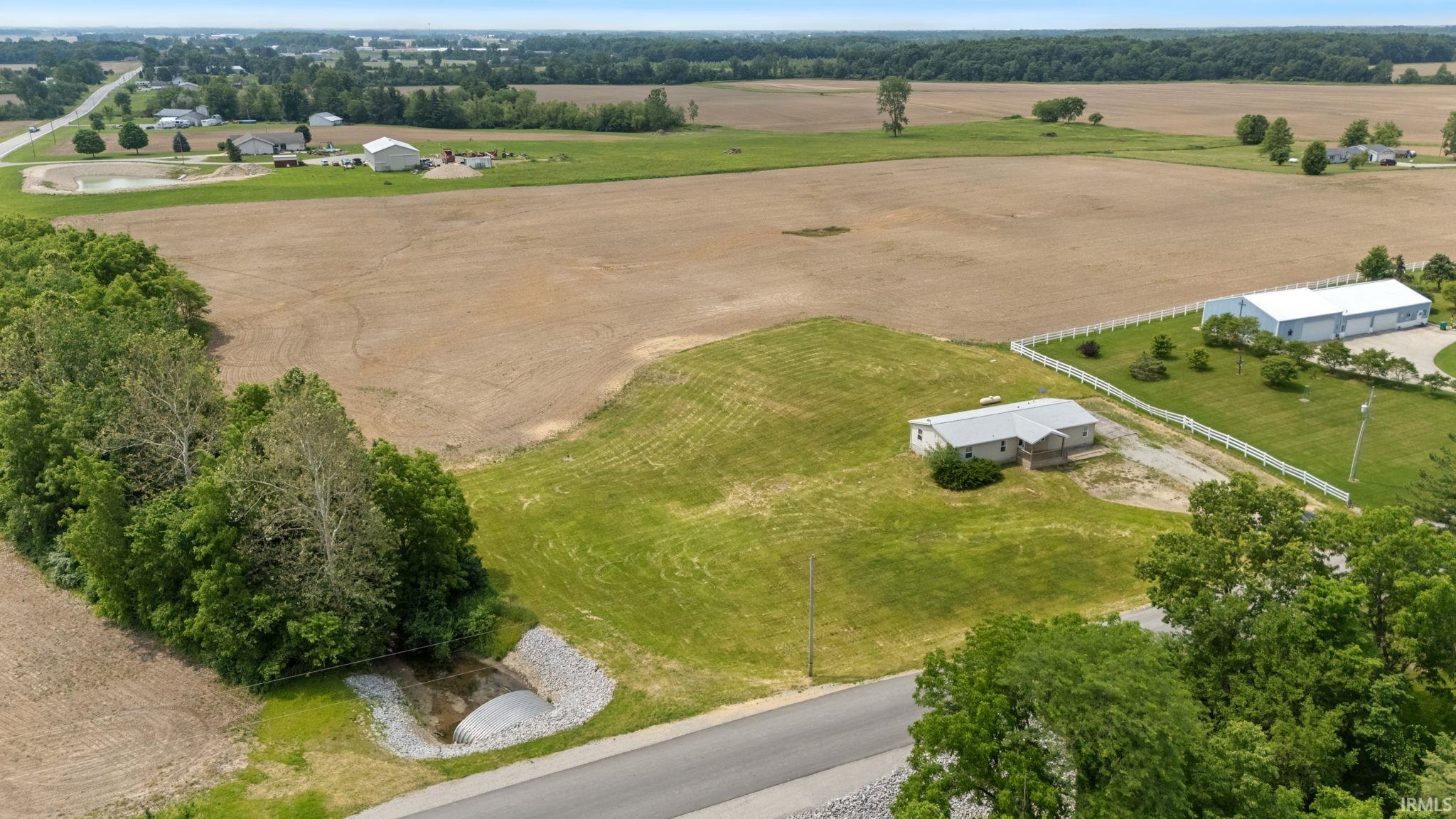 Spacious property featuring a single-story residence, a large outbuilding, a white perimeter fence, and extensive open land
