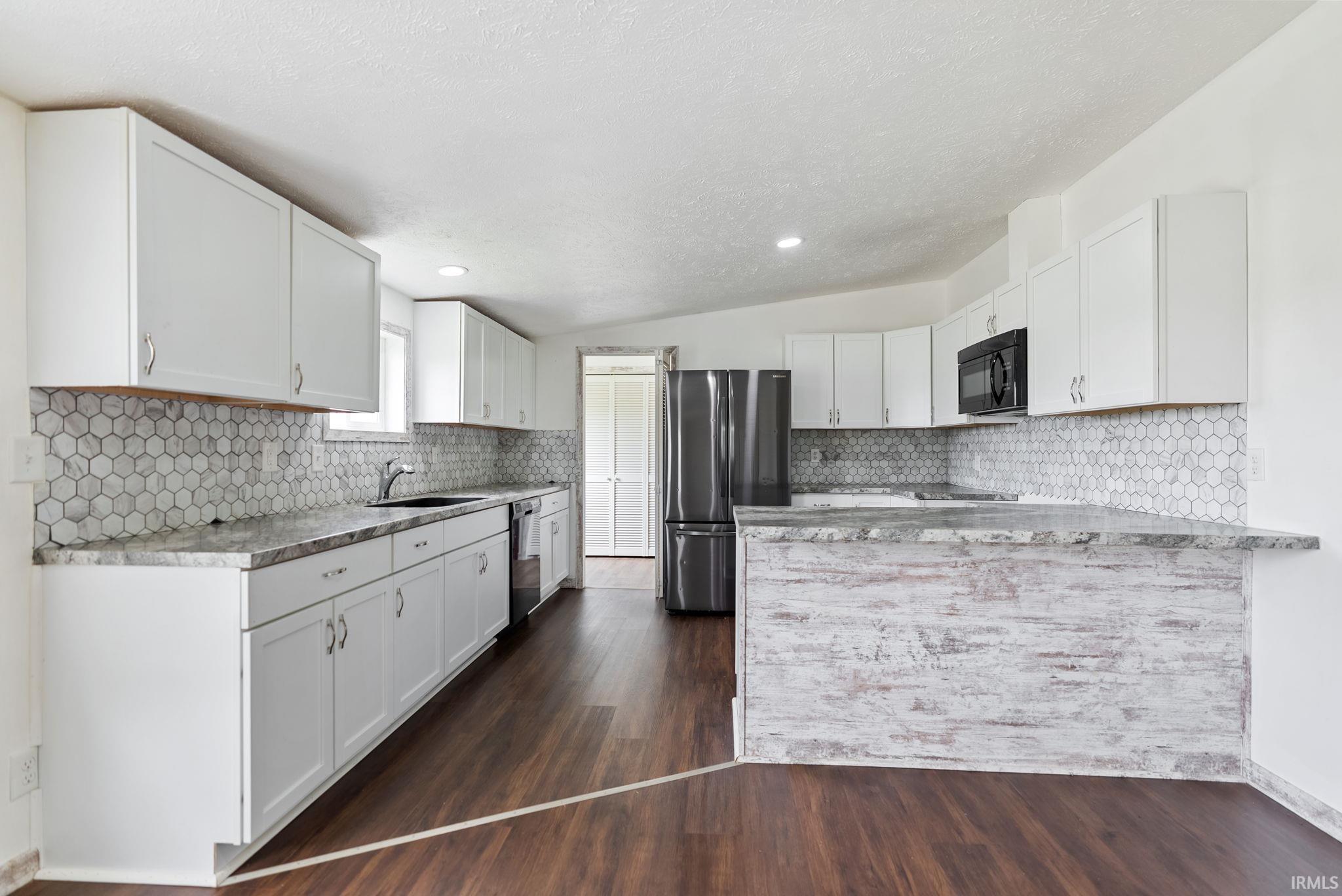 Kitchen featuring white cabinetry, hexagon tile backsplash, dark countertops, wood-finish flooring, and a stainless steel refrigerator