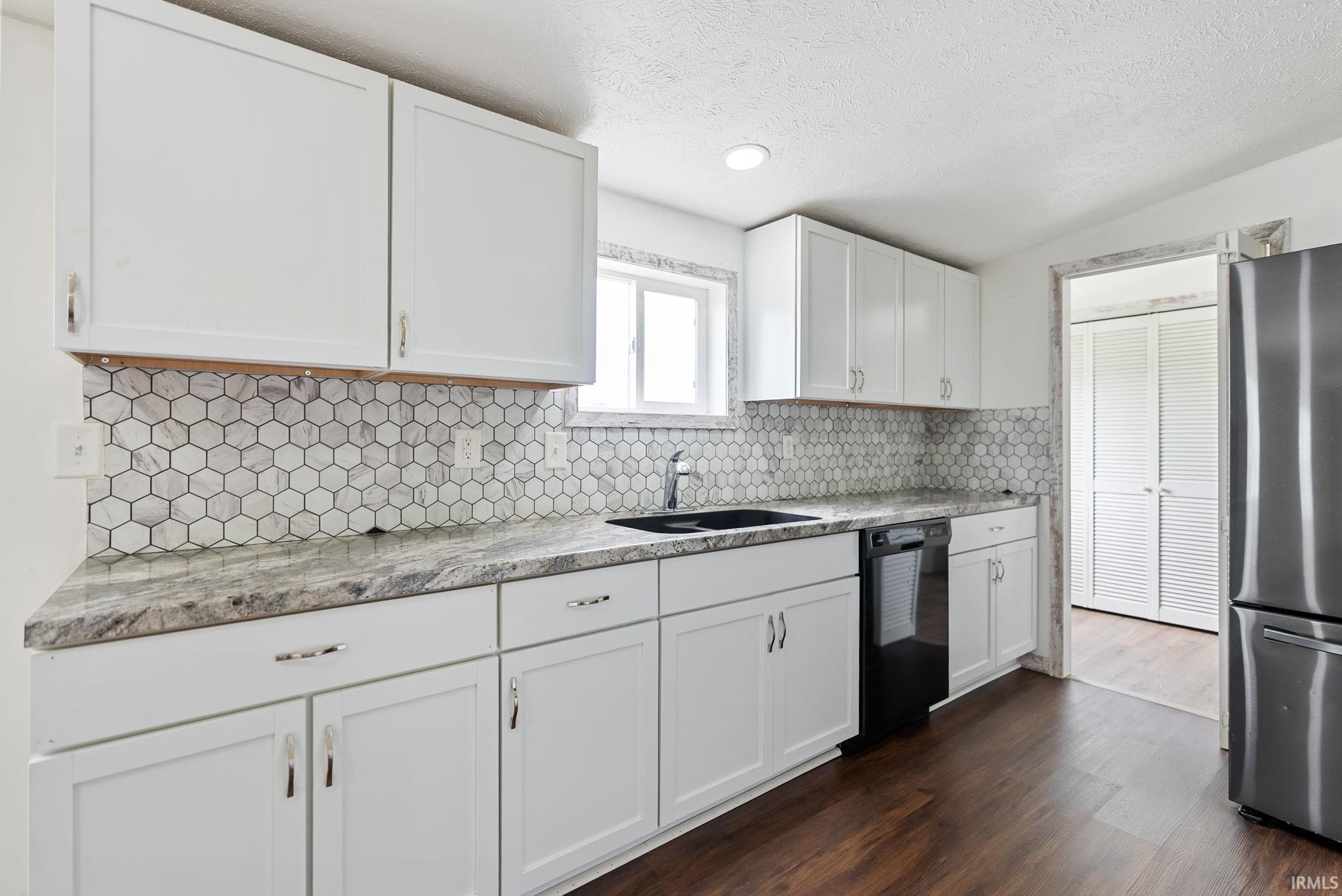 Kitchen featuring white cabinetry with brushed nickel hardware, a hexagon tile backsplash, and wood-finish flooring