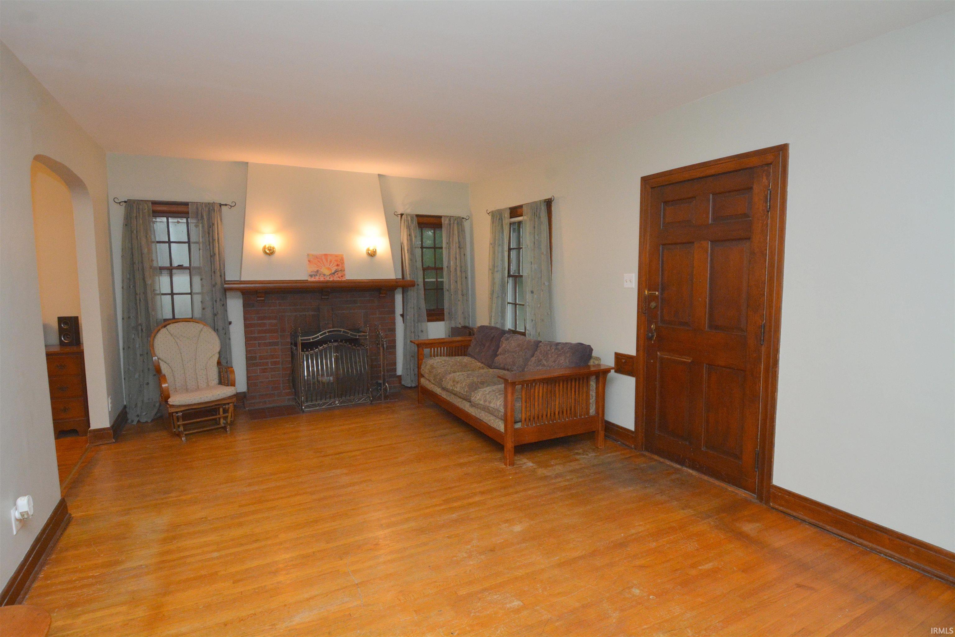 Living area featuring rich wood-finish flooring, a brick fireplace with a wood mantle, and sconce lighting