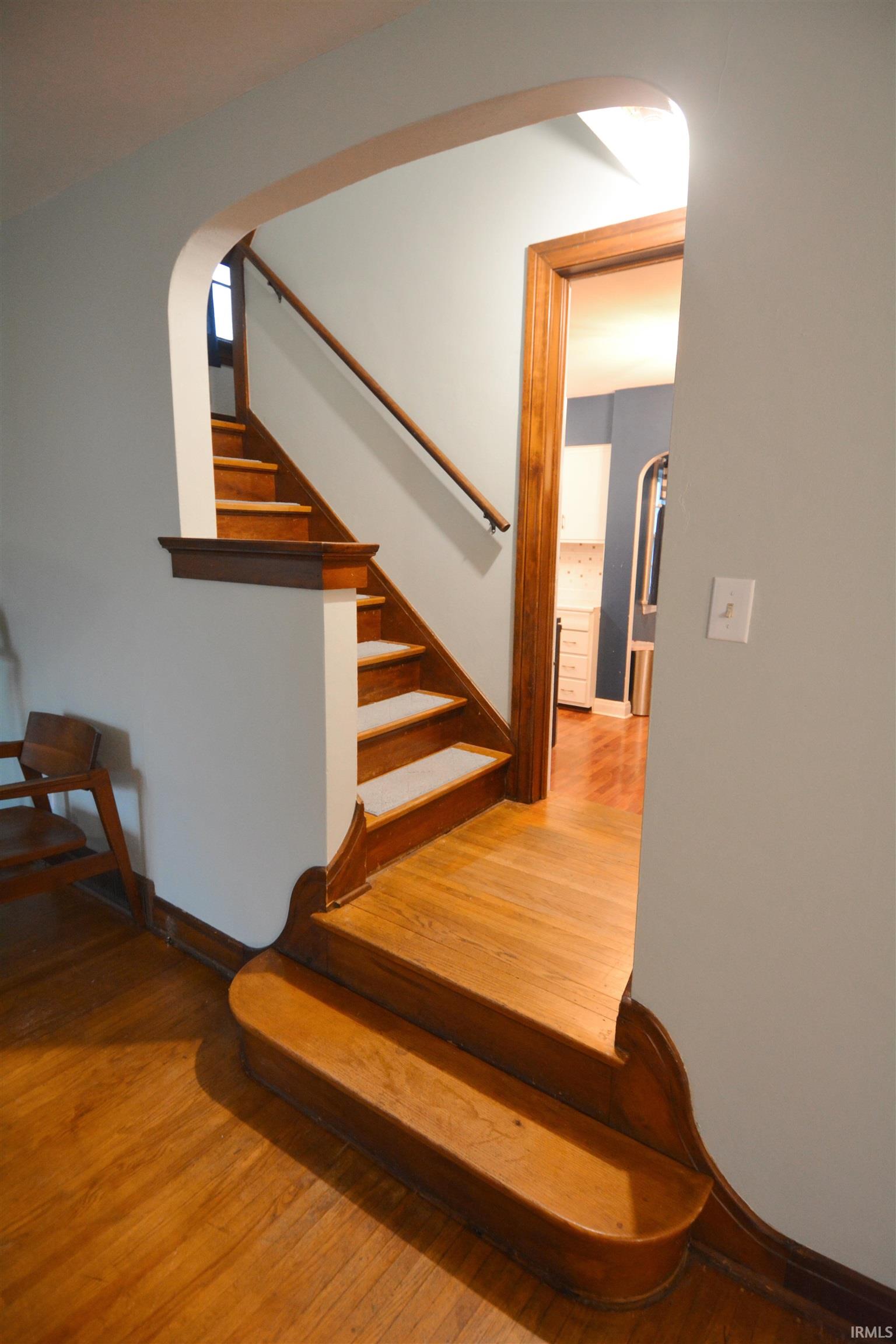 Arched entryway featuring warm wood-finish flooring, a coordinating wooden staircase with carpeted treads, and classic wood trim details